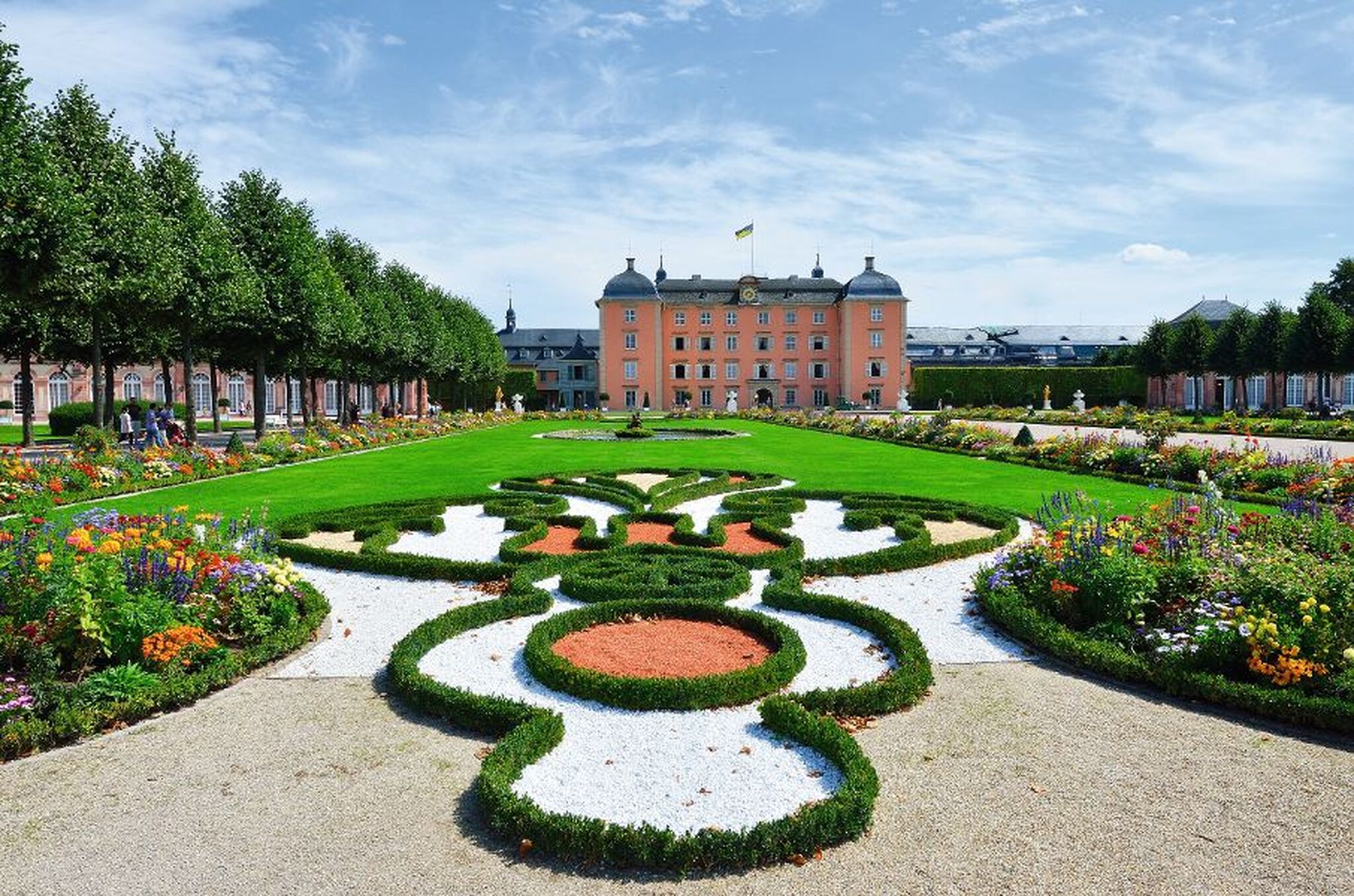 Barockgarten vor einem rosa Schloss bei klarem Himmel.