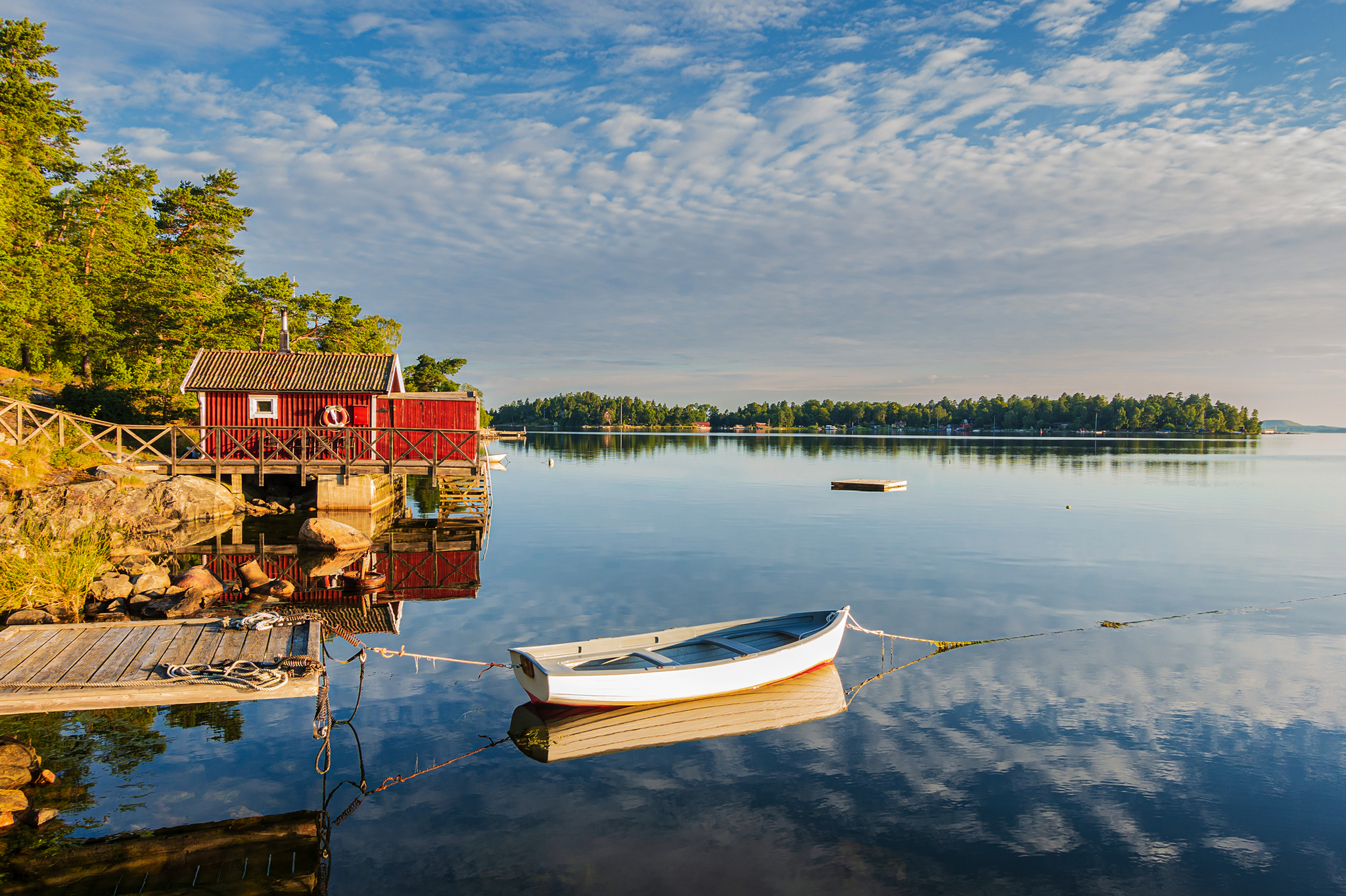 Boot am Steg vor rotem Haus an einem See bei klarem Himmel.