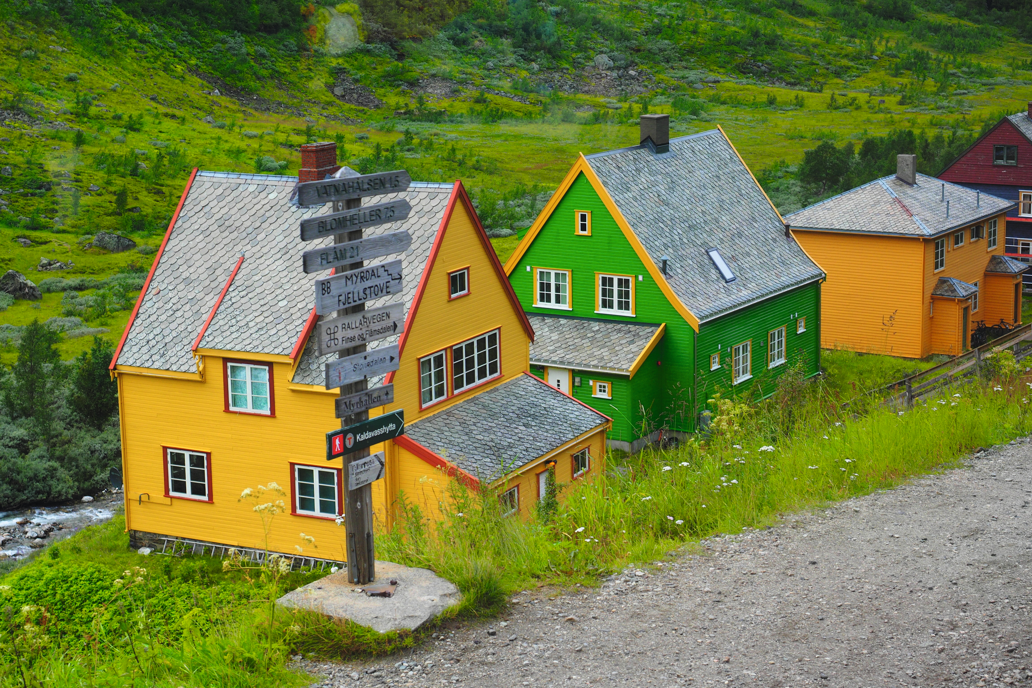 Bunte Holzhäuser in einer ländlichen Landschaft mit Weg und Bäumen.