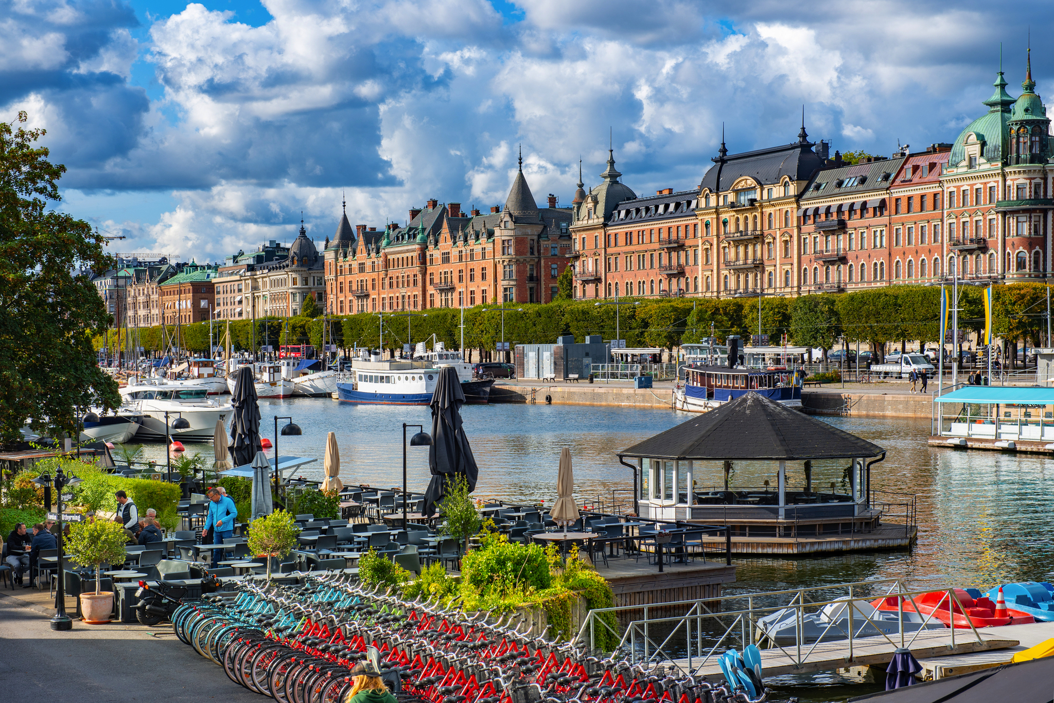 Uferpromenade mit Fahrrädern, Geschäften und historischen Gebäuden am Wasser.
