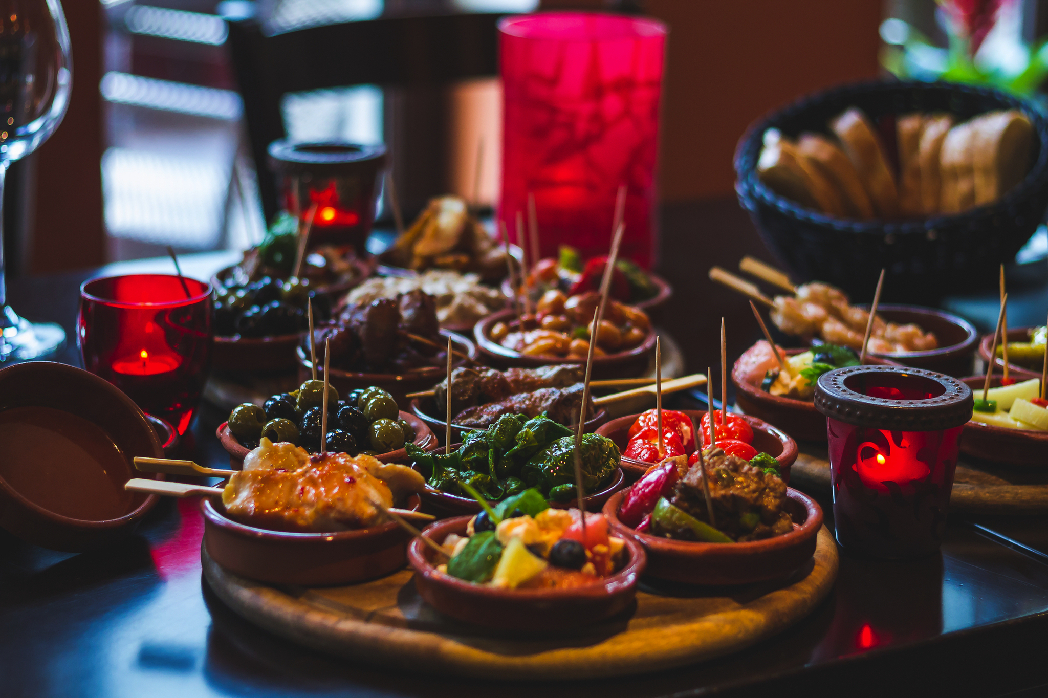 Verschiedene Tapas auf einem Tisch mit Kerzen und Brot im Hintergrund.