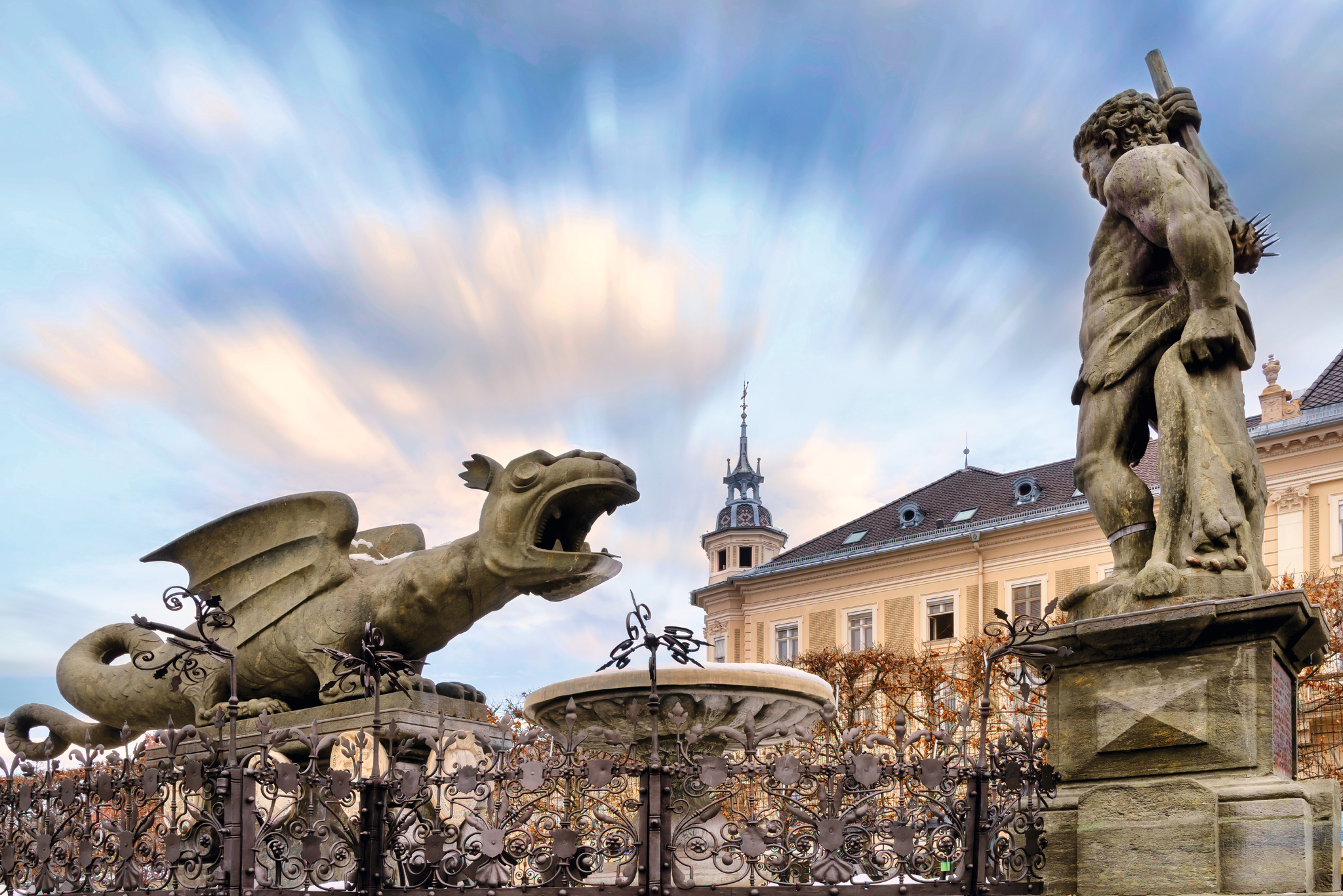 Steinstatue eines Drachen und eines Mannes vor historischer Gebäudekulisse.