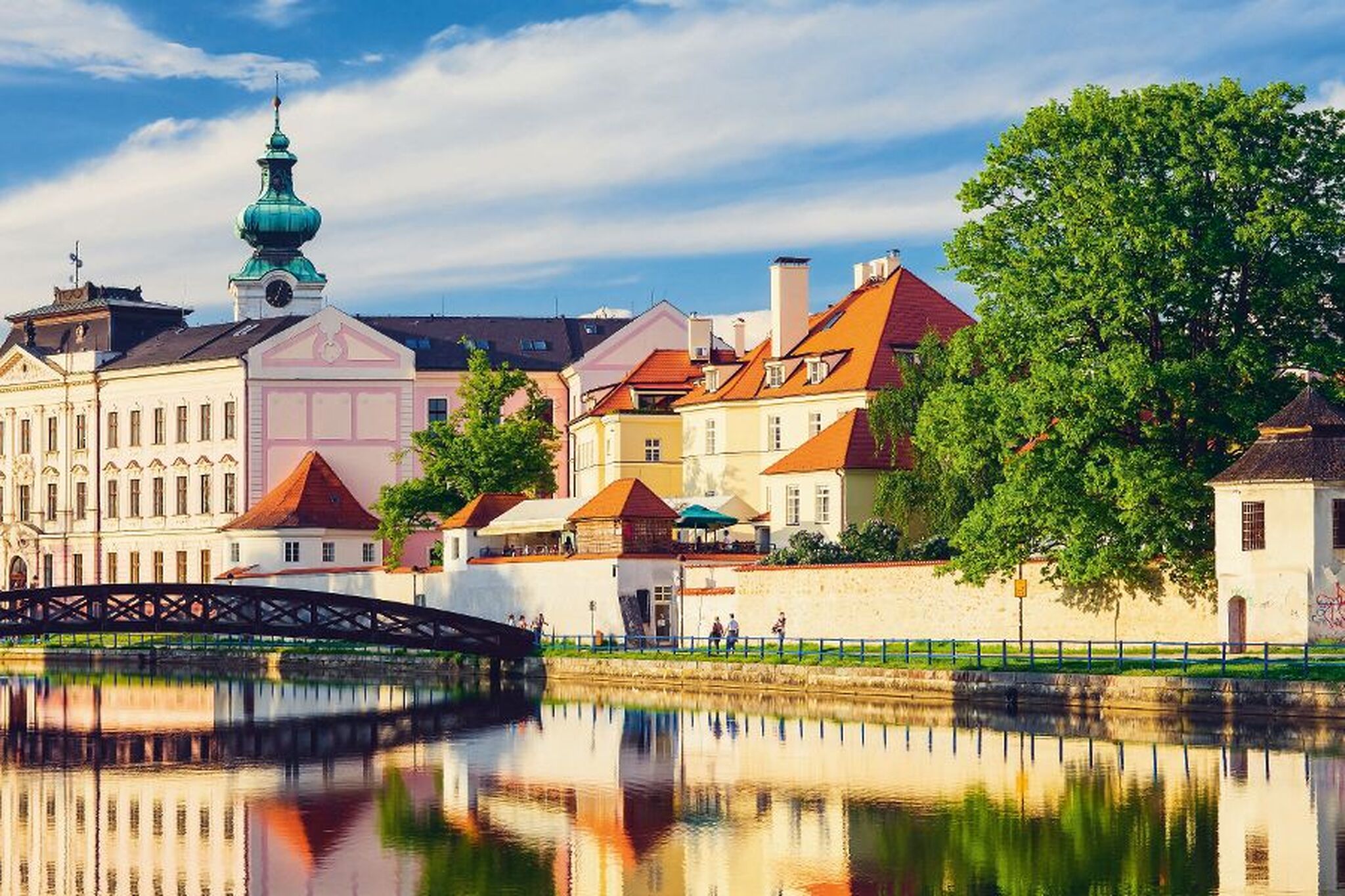 Bunte historische Gebäude mit Baum und Fluss im Vordergrund.