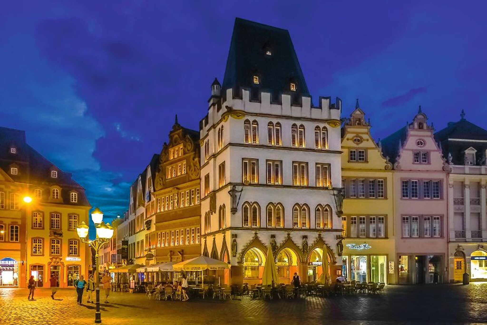 Historisches Gebäude bei Nacht auf einem belebten Platz mit Cafébesuchern.