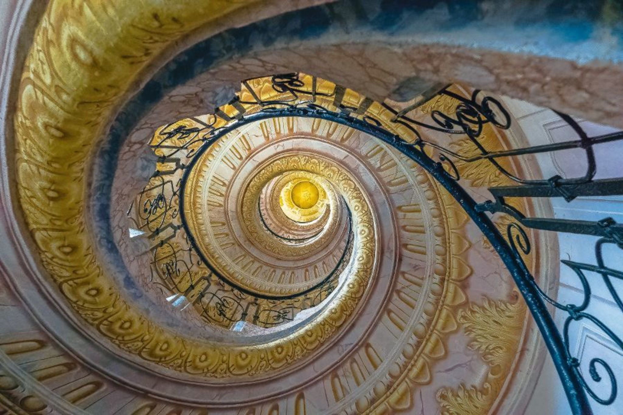 Blick nach oben in ein kunstvoll verziertes Wendeltreppenhaus mit geschmiedetem Geländer.