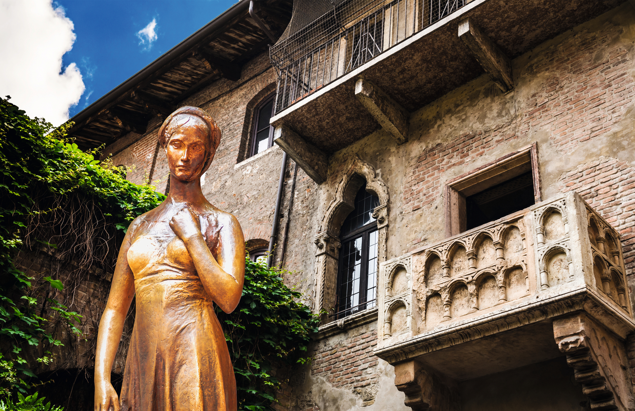 Statue einer Frau vor einem historischen Gebäude mit Balkon und Efeu.