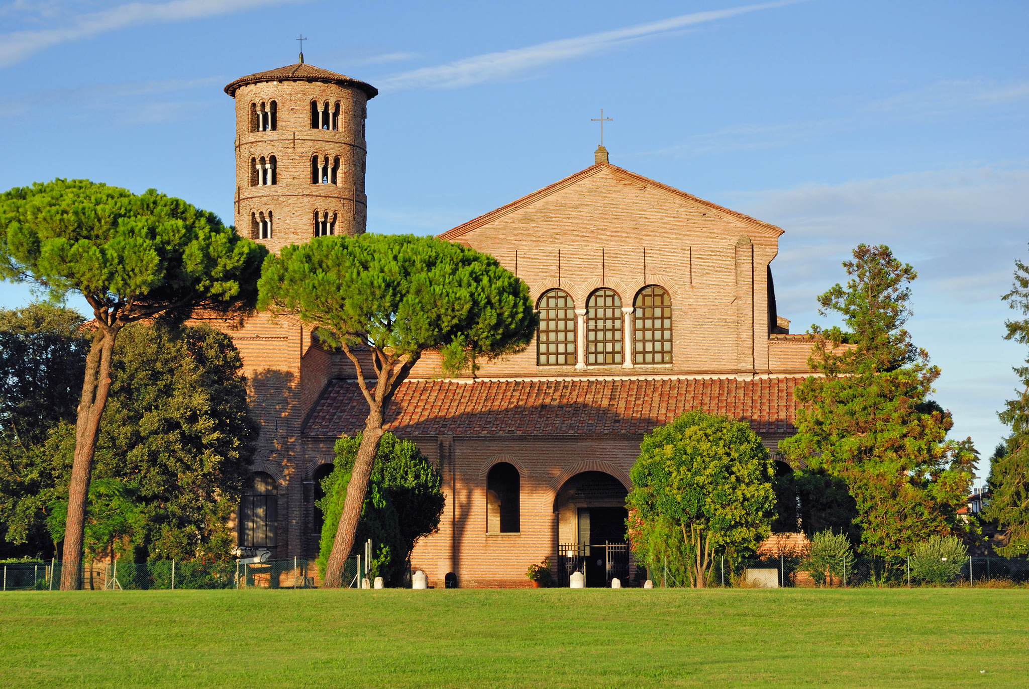 Kirche mit Rundturm, umgeben von Bäumen, bei klarem Himmel.
