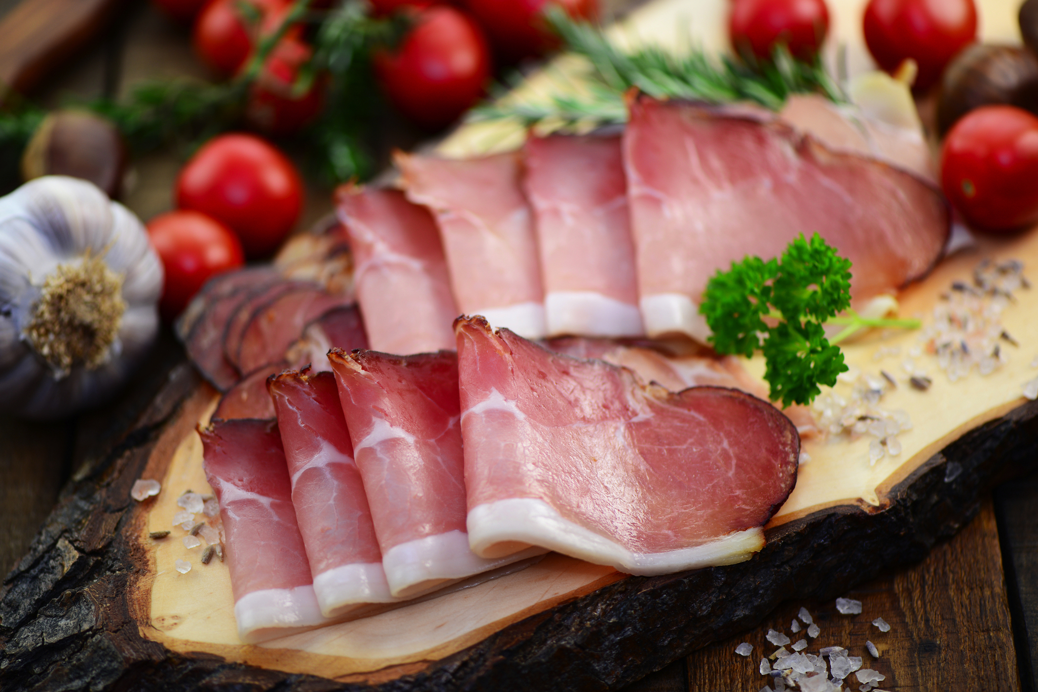 Aufgeschnittener Schinken auf Holzbrett mit Tomaten und Knoblauch