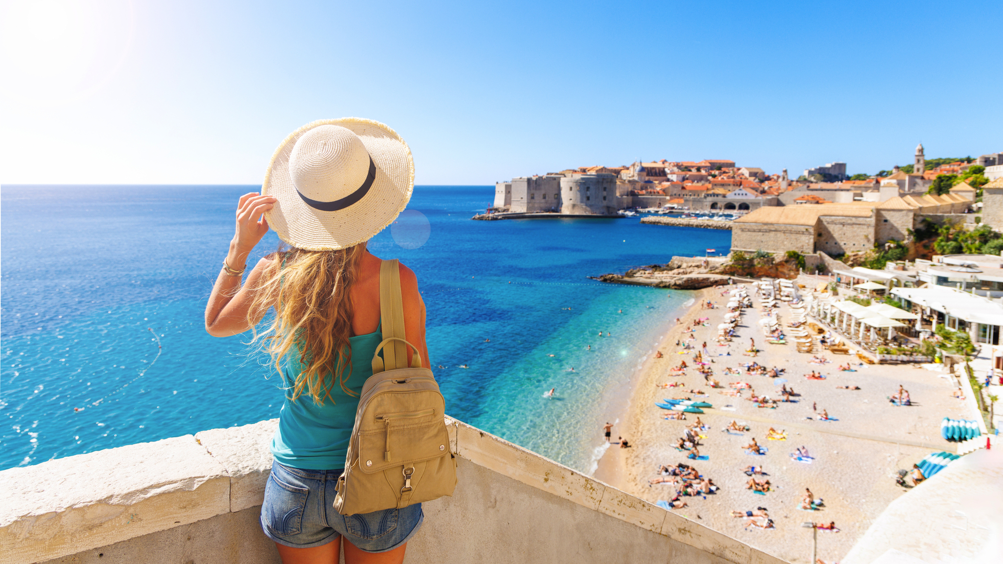 Frau in Sommerkleidung blickt auf Küste und Altstadt am Meer