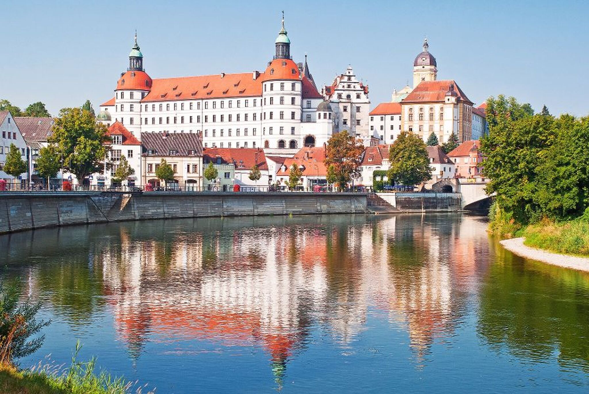 Historisches Schloss an einem Flussufer mit Spiegelung im Wasser.