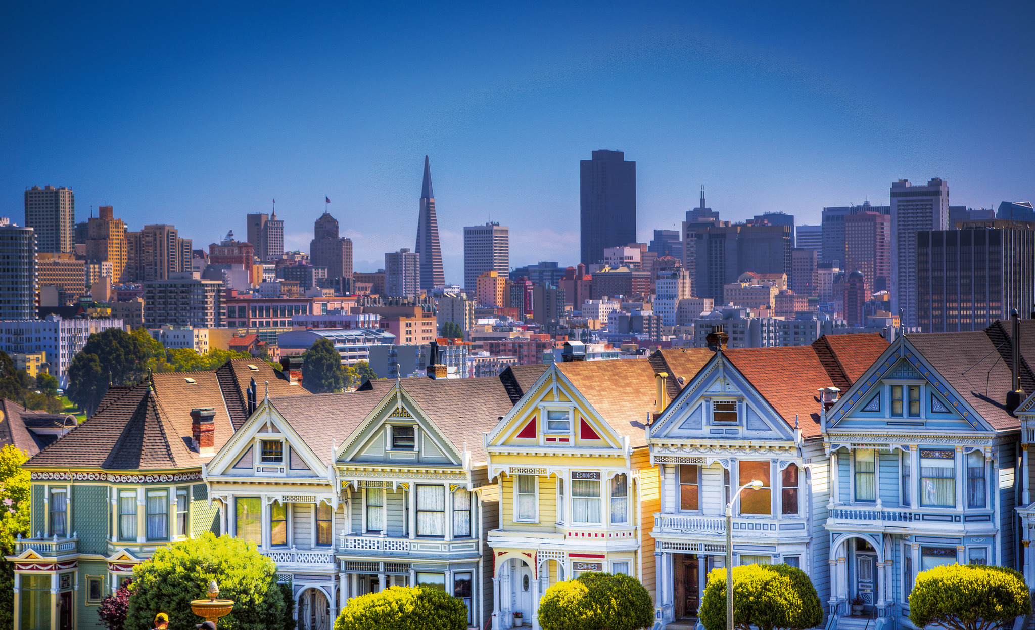 Reihe bunter viktorianischer Häuser vor der Skyline einer Stadt.