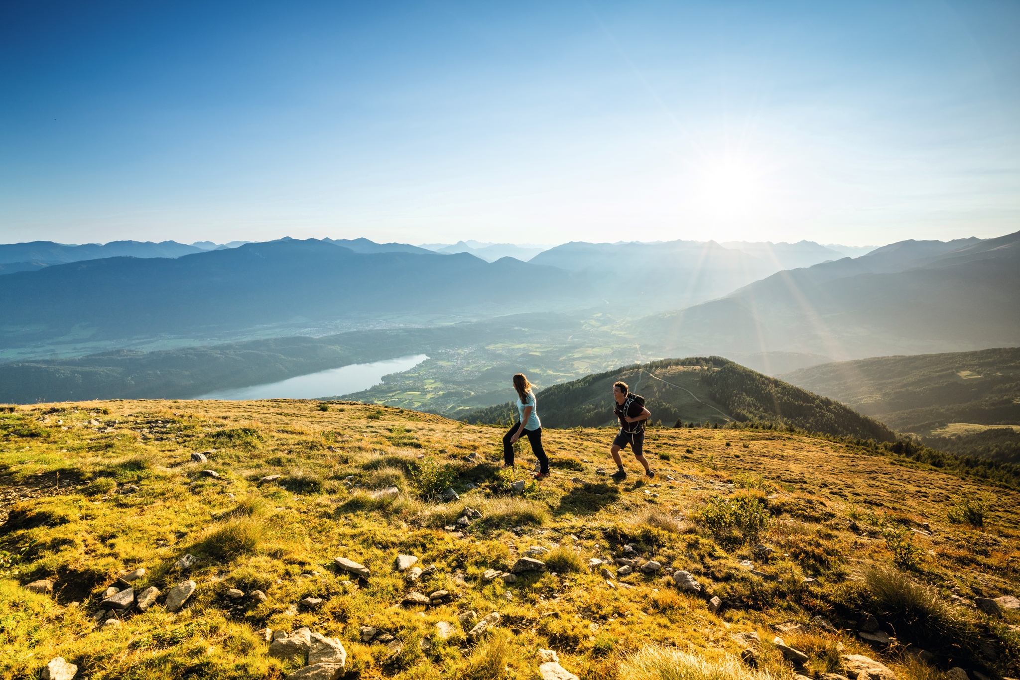 Zwei Wanderer auf einem Hügel mit Blick auf den Millstätter See bei Sonnenschein.