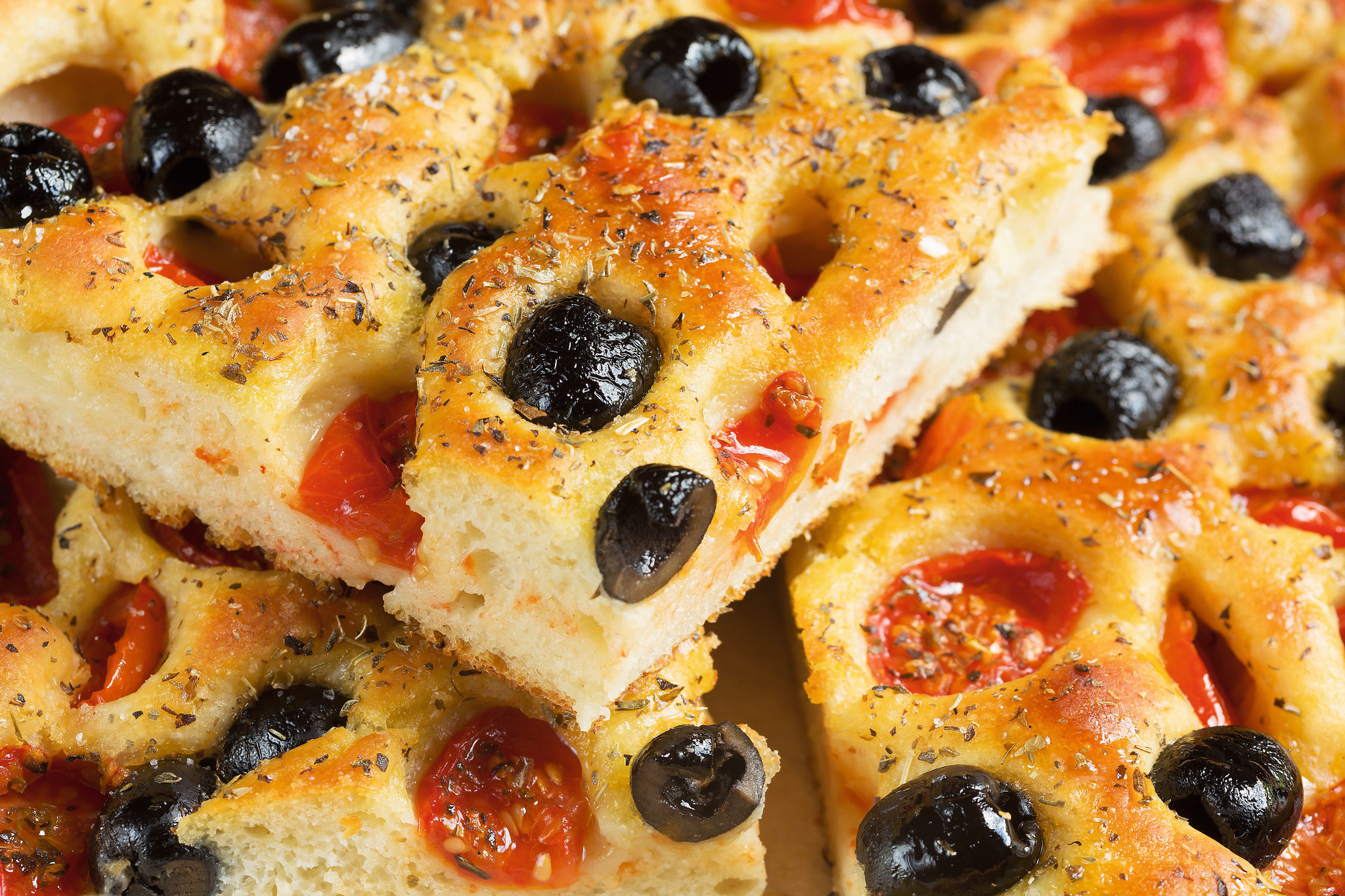 Focaccia-Brot mit schwarzen Oliven und getrockneten Tomaten, bestreut mit Kräutern.