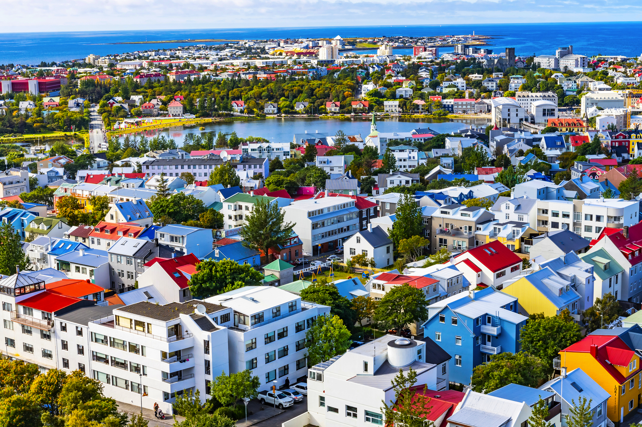 Stadtpanorama mit bunten Häusern, Bäumen und einem See im Hintergrund.