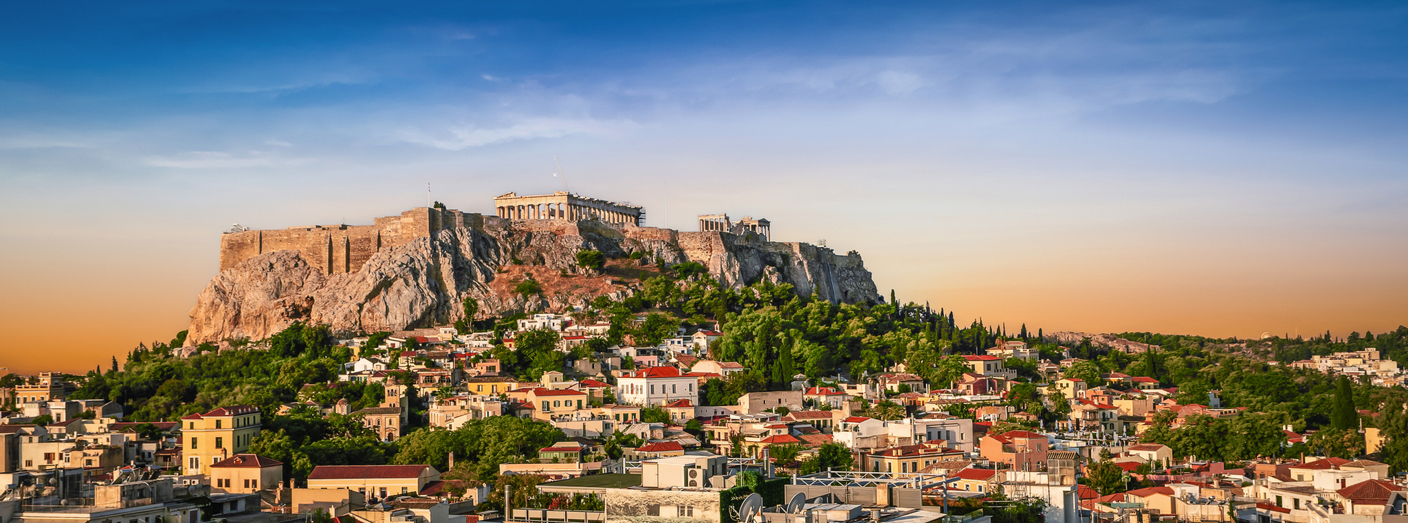 Blick auf die Akropolis in Athen bei Sonnenuntergang, umgeben von Stadt und Natur.