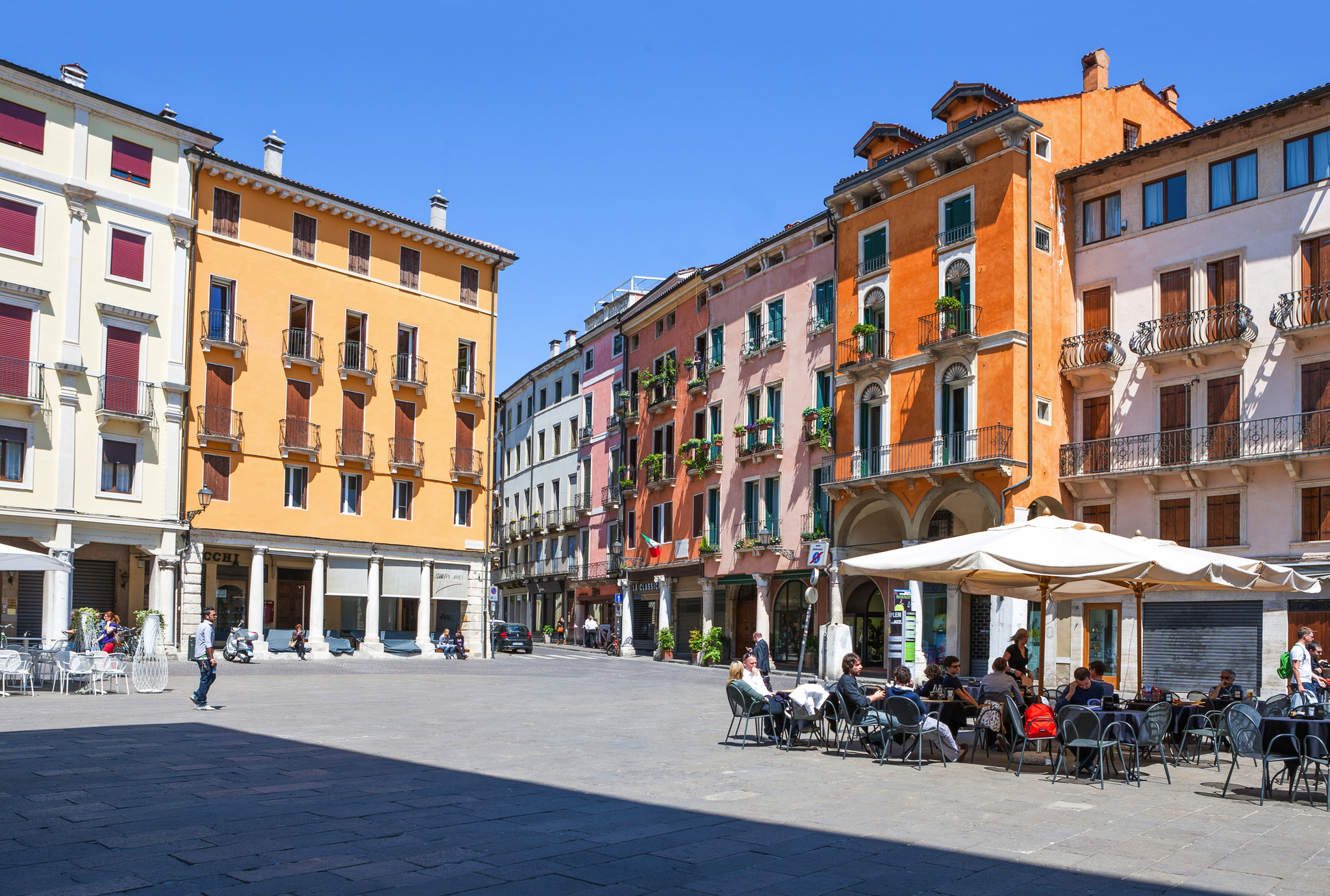 Städtischer Platz mit historischen bunten Gebäuden und Straßencafé bei sonnigem Wetter.