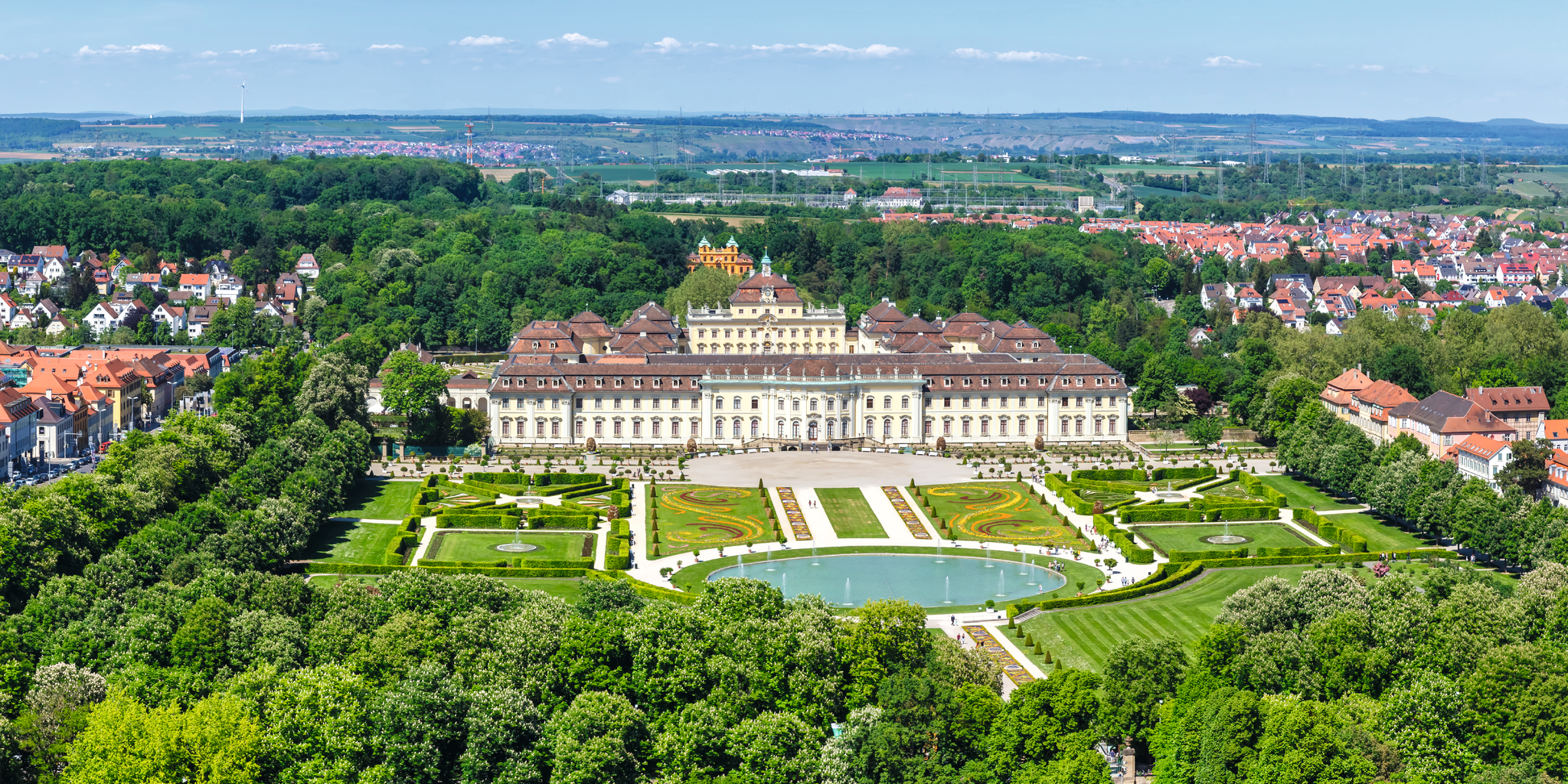 Luftaufnahme eines großen Schlosses mit symmetrischen Gärten und Springbrunnen.