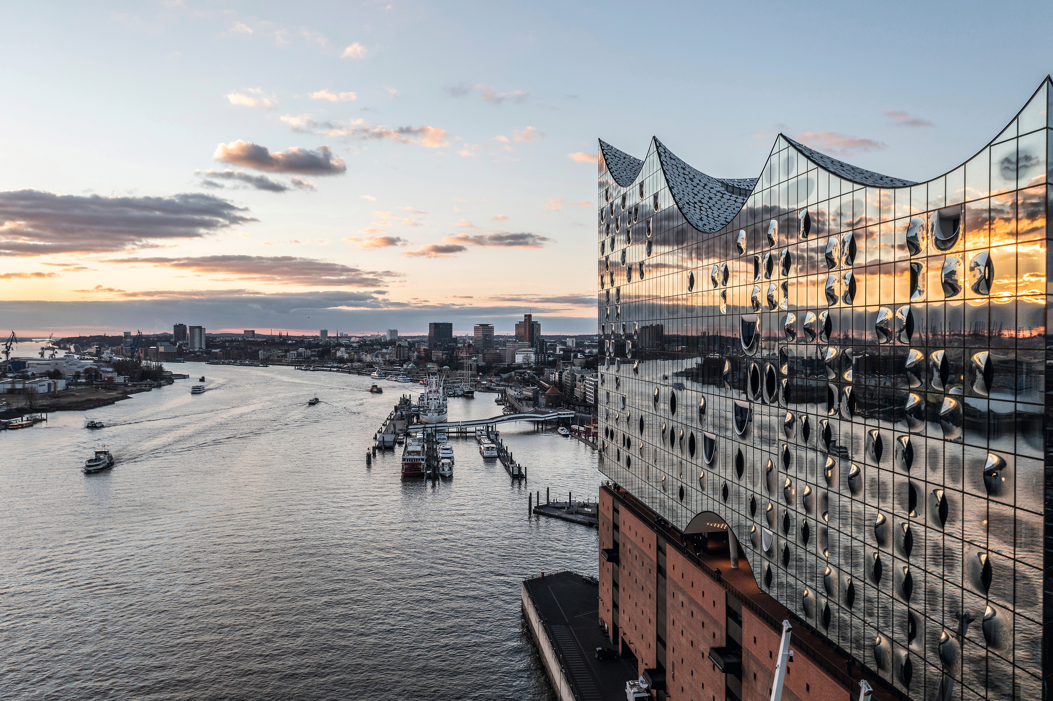 Blick auf die Elbphilharmonie in Hamburg bei Sonnenuntergang, Hafen und Elbe im Hintergrund.