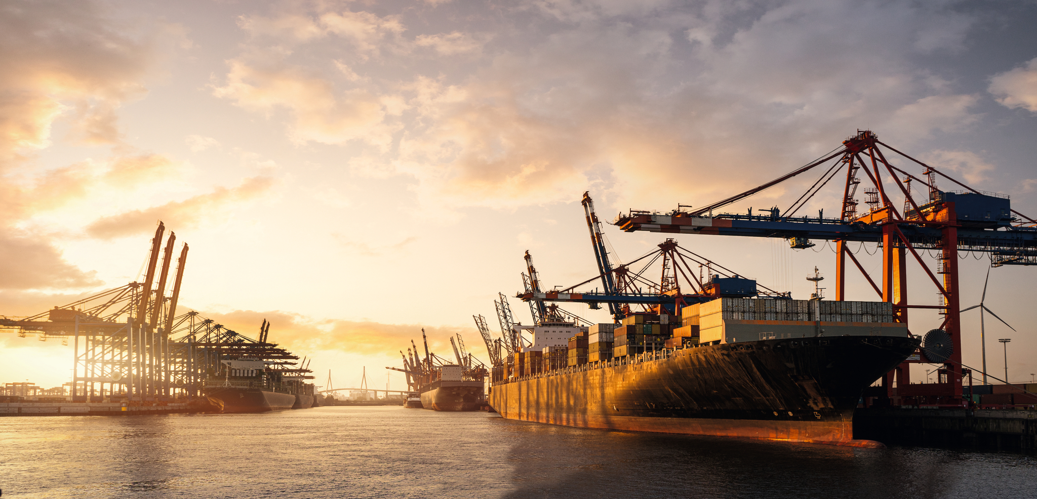 Frachtschiffe und Kräne im Hafen bei Sonnenuntergang