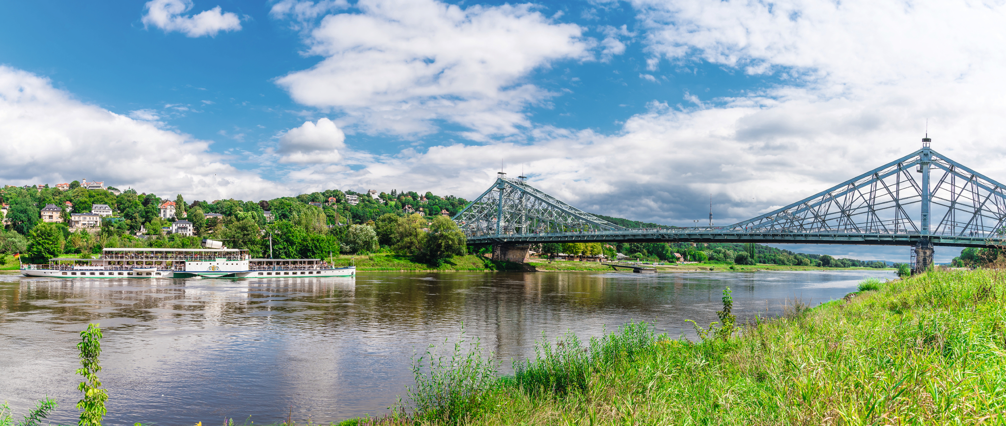 Blauer Himmel, Fluss, Schaufelraddampfer, historische Brücke, grüne Ufervegetation