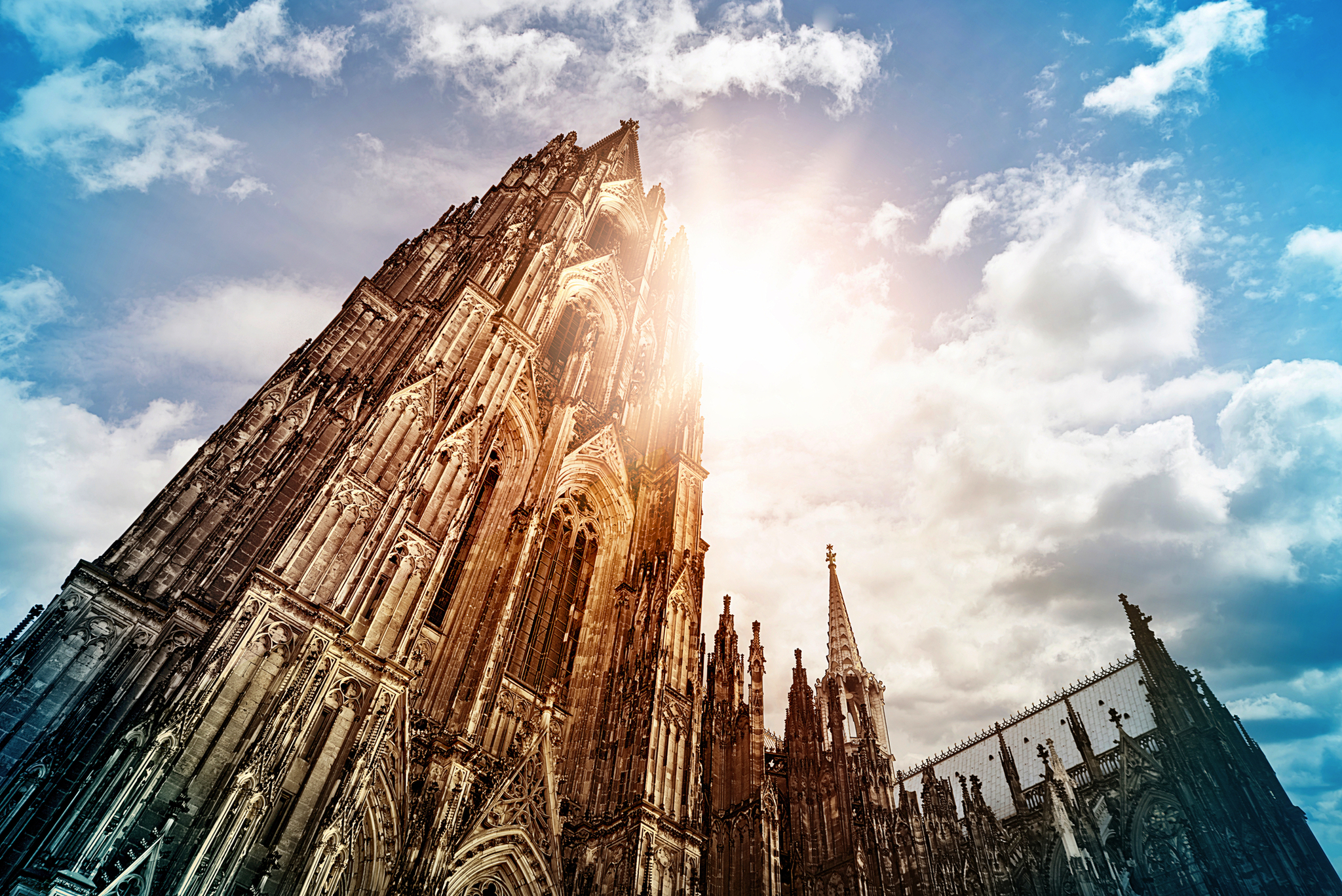 Sonnenschein hinter einer gotischen Kathedrale mit Wolken am Himmel.