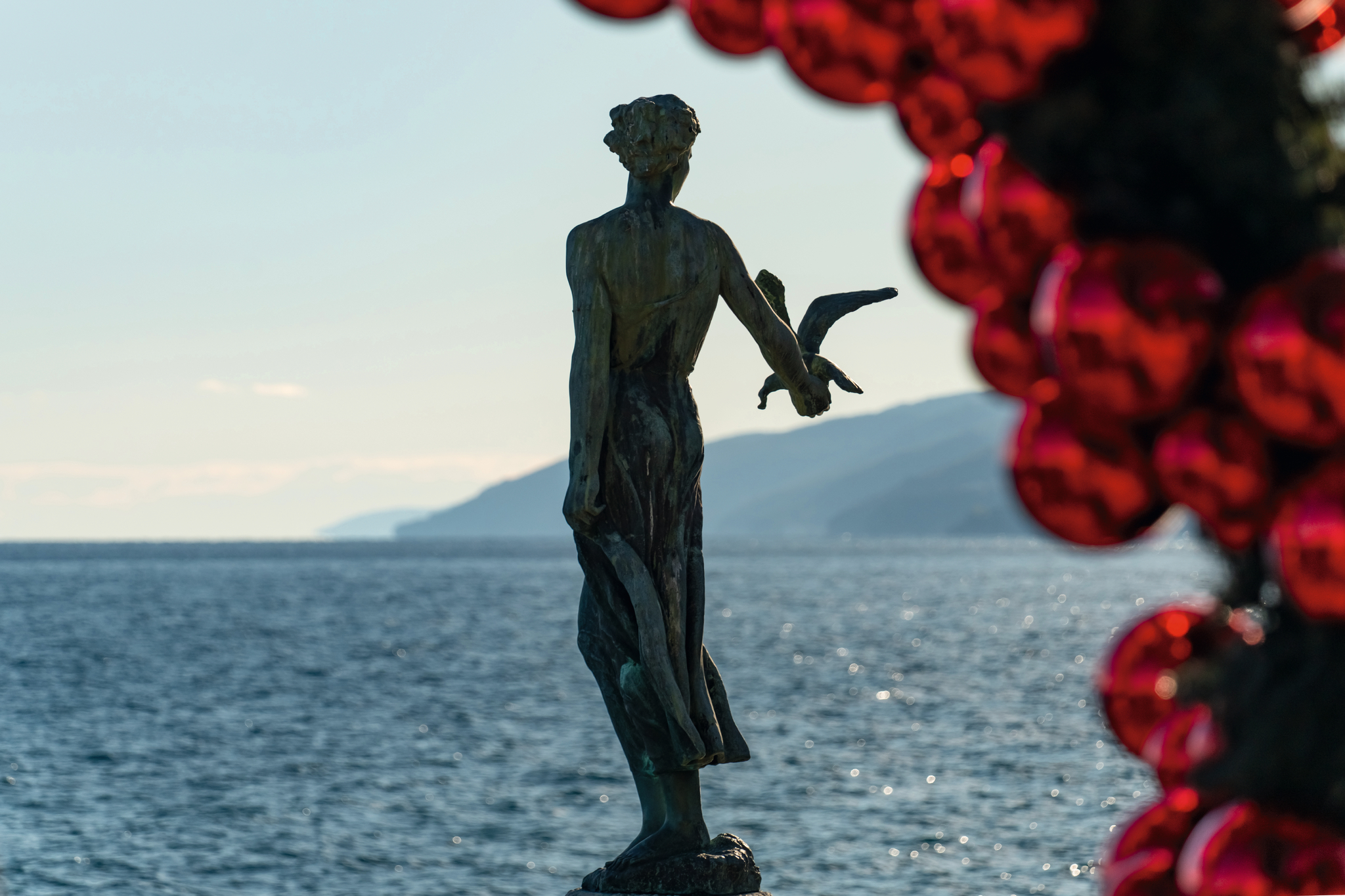 Statue am Meer mit roten Dekorationen im Vordergrund.