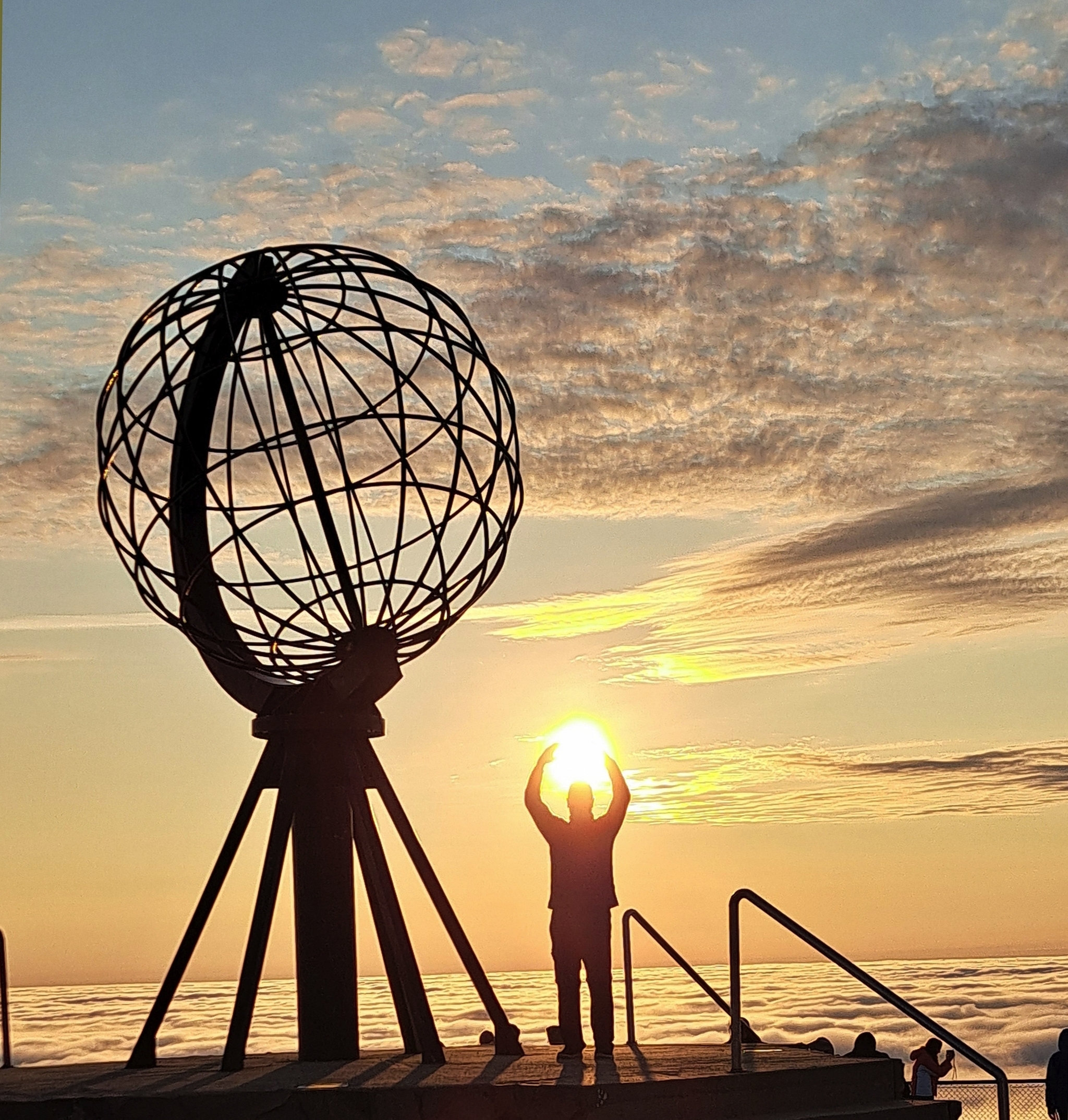 Person beim Globus-Denkmal am Nordkap, der die Sonne hält, im Sonnenuntergang.