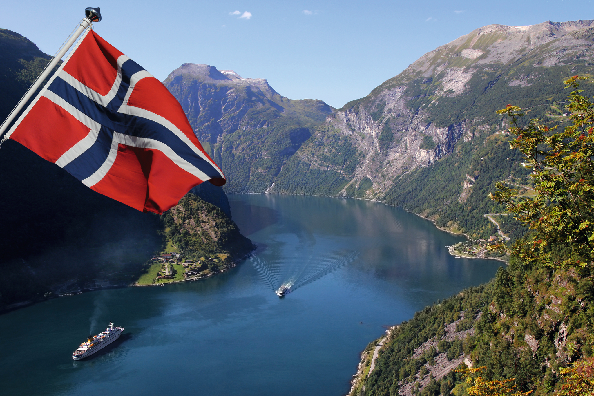 Norwegische Flagge über Fjordlandschaft mit Booten und Bergen im Hintergrund.