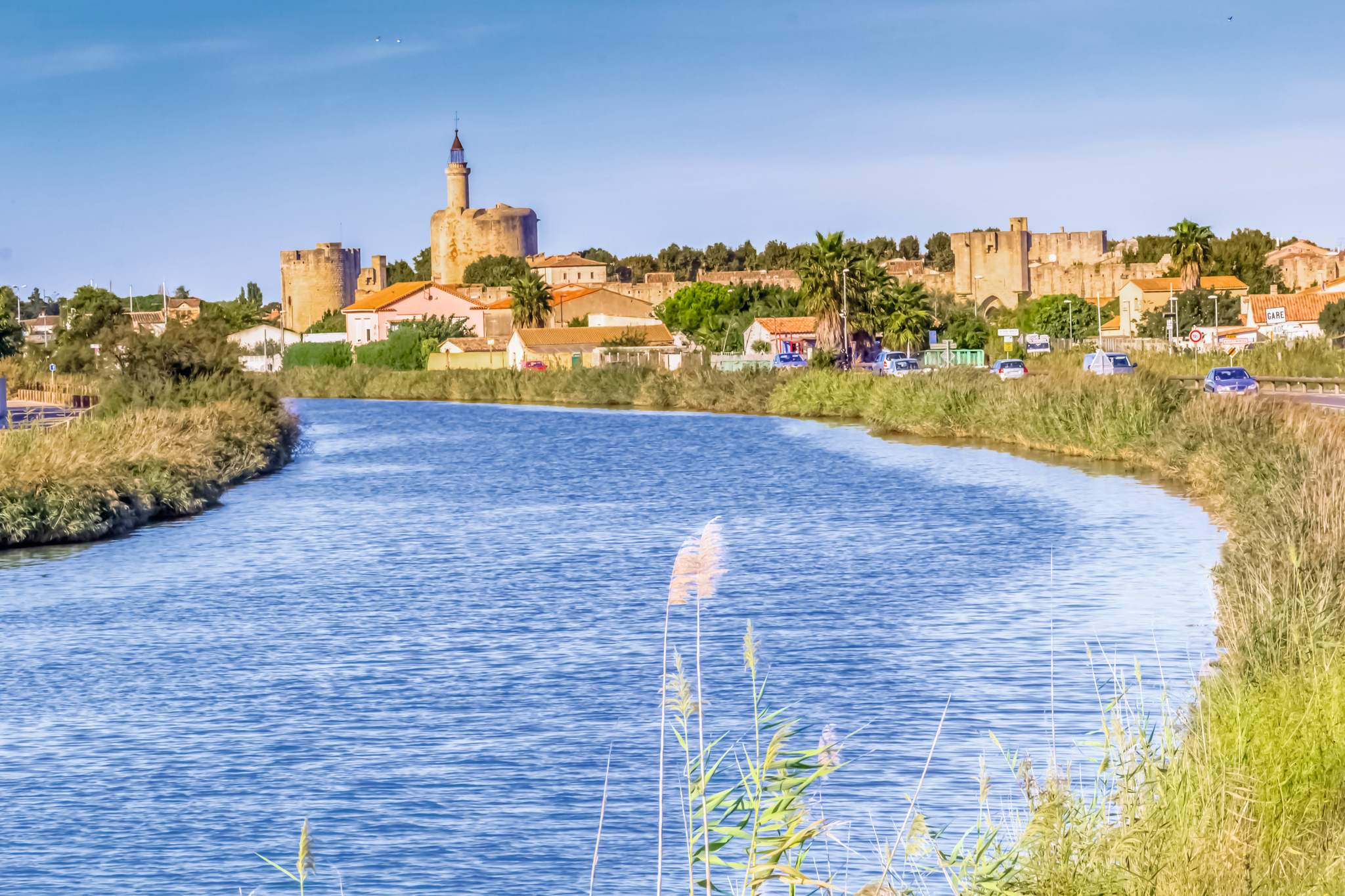Stadtansicht mit Burgtürmen und Fluss im Vordergrund bei Sonnenschein.