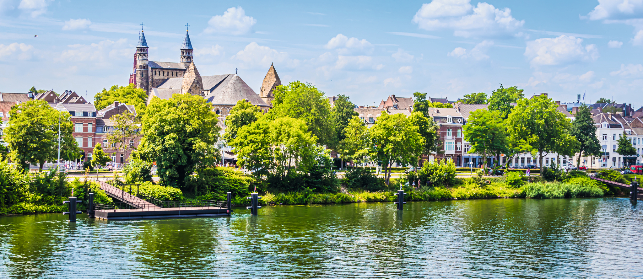 Stadtansicht mit Kirche und Fluss unter blauem Himmel.