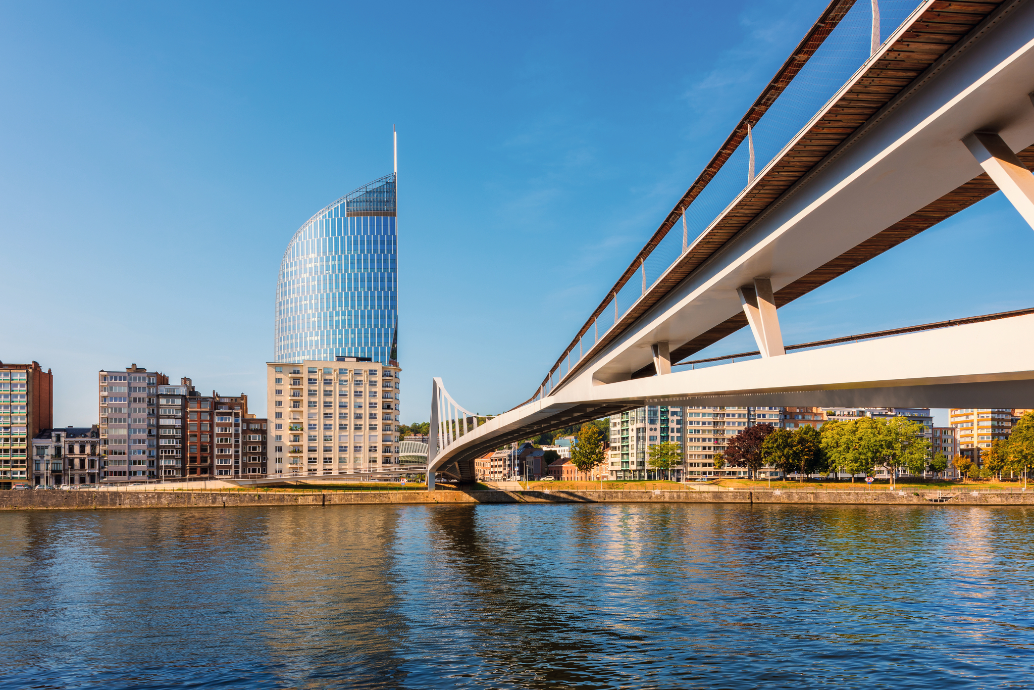 Moderne Glasgebäude und elegante Brücke an einem Flussufer bei klarem Himmel.