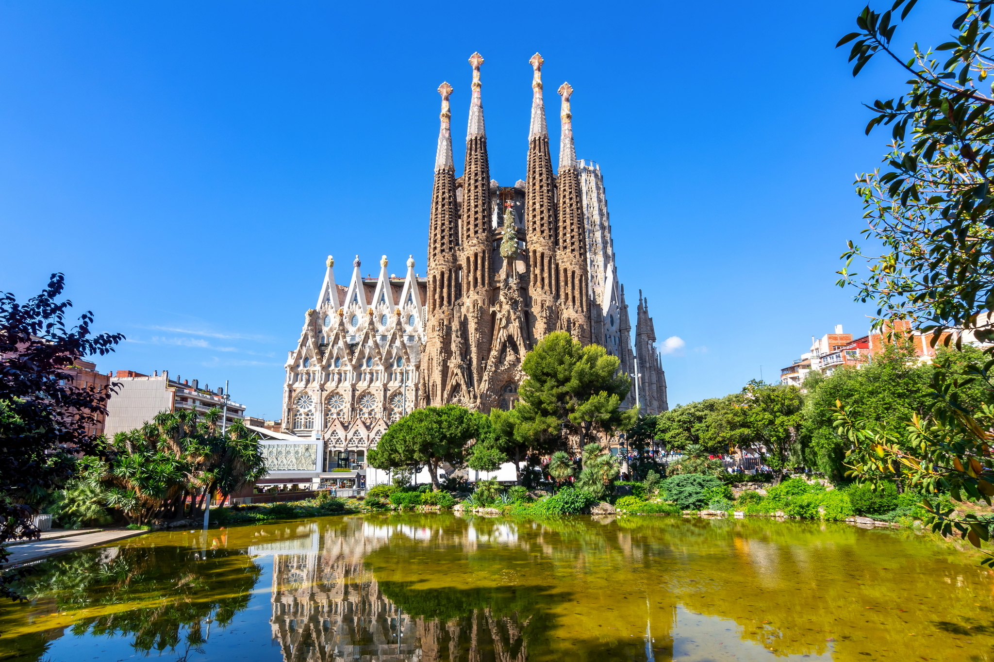 Sagrada Família in Barcelona bei klarem Himmel mit Spiegelung im Wasser.