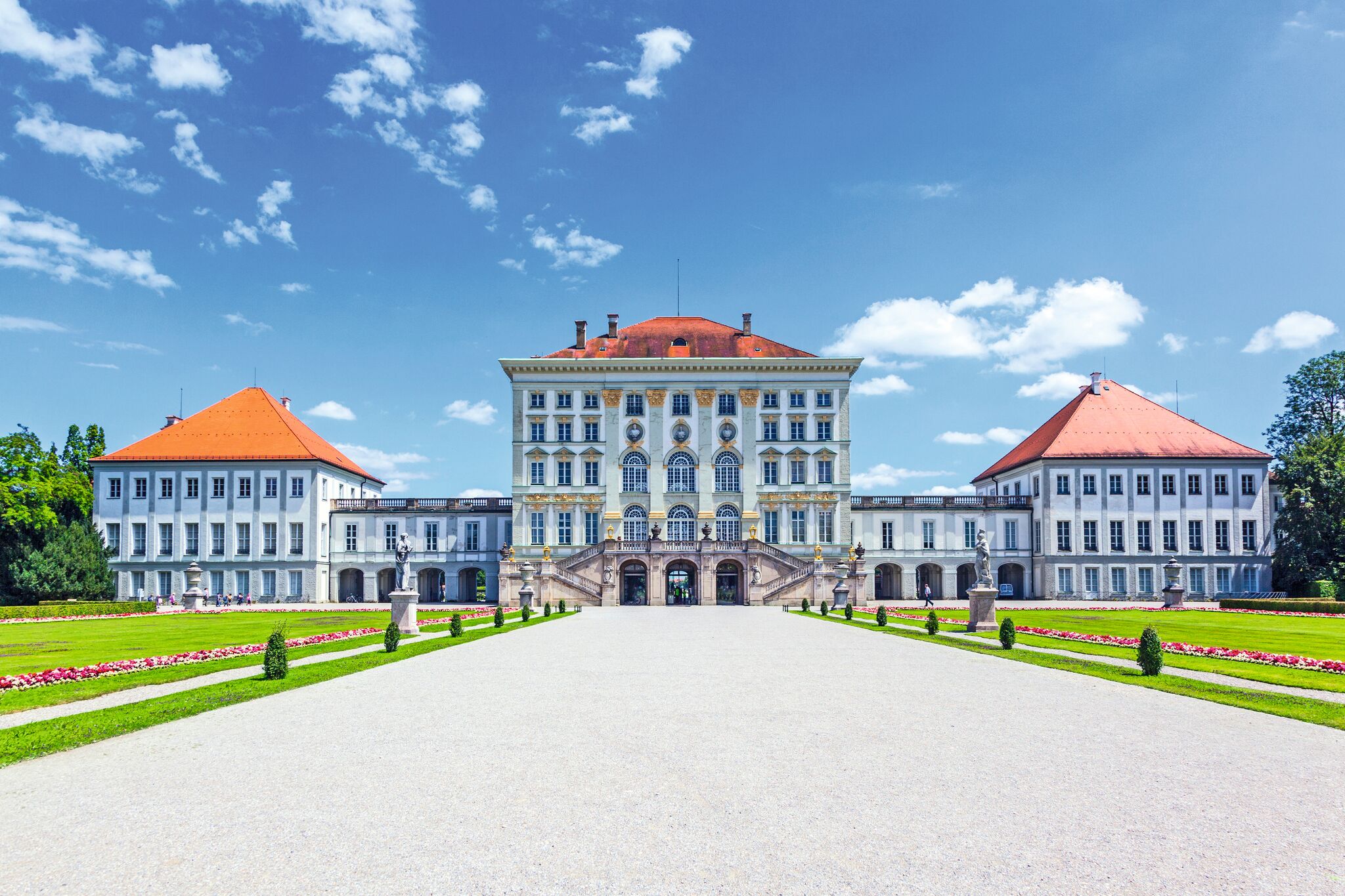 Barockschloss mit rotem Dach und symmetrischem Garten unter blauem Himmel.
