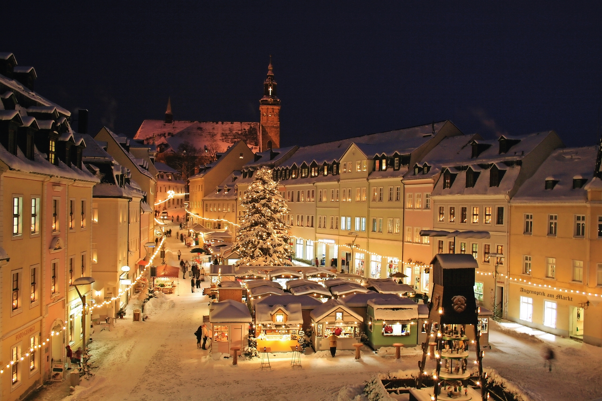 Verschneiter Weihnachtsmarkt in einer beleuchteten Altstadt bei Nacht.