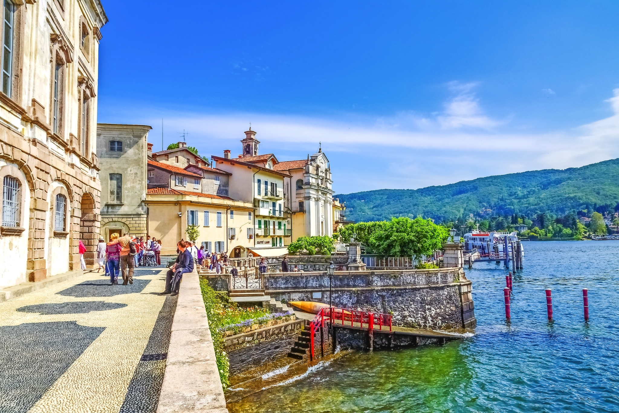 Menschen spazieren an der Uferpromenade eines malerischen Sees.