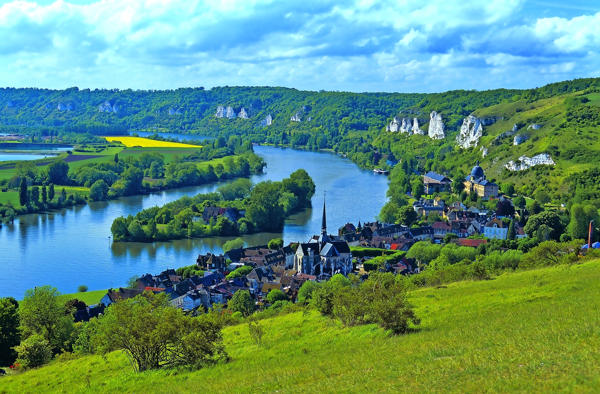 Landschaft mit Fluss, Hügeln und Dorf im Vordergrund.