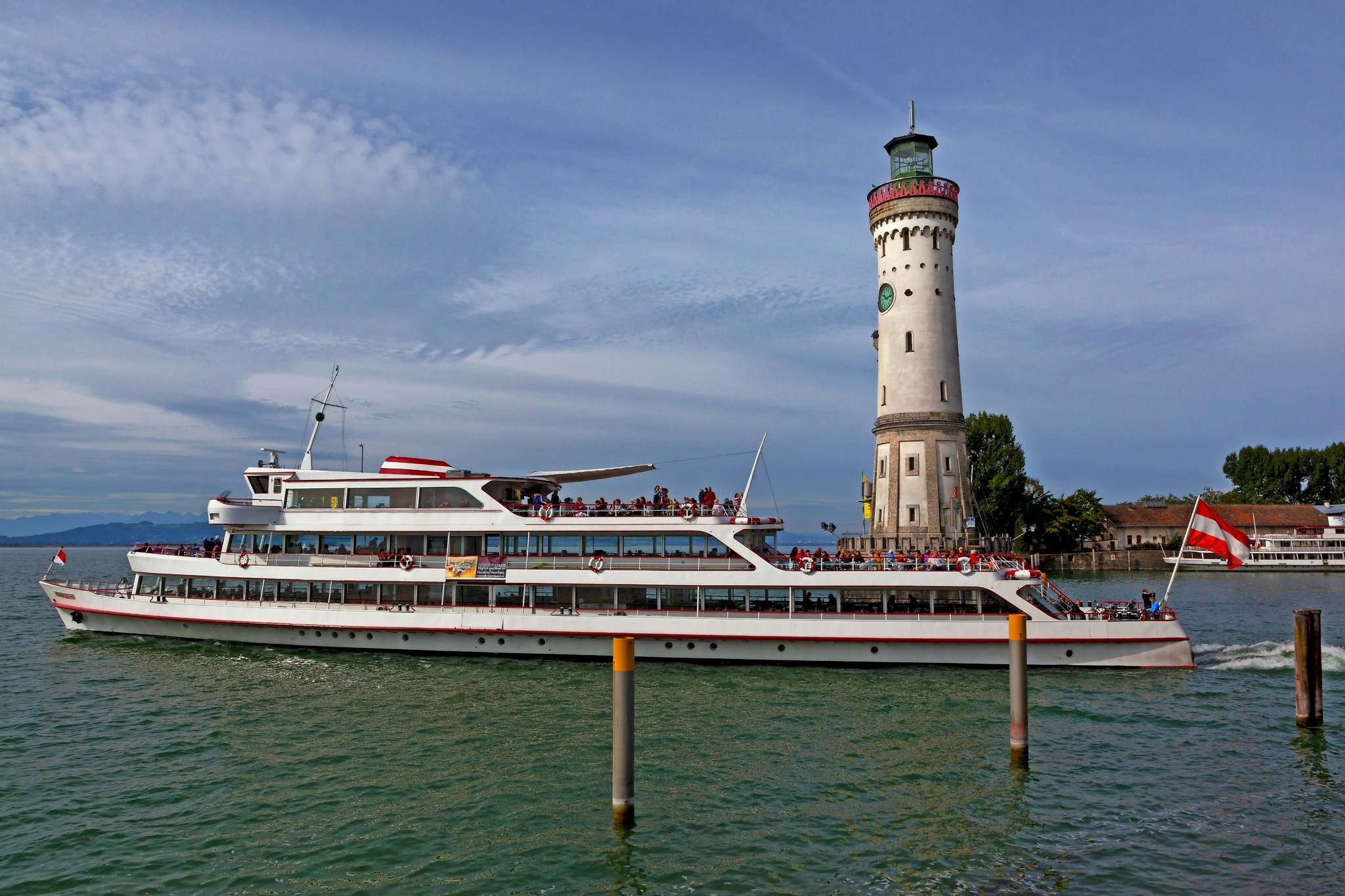Ein Ausflugsschiff fährt an einem Leuchtturm auf einem See vorbei.