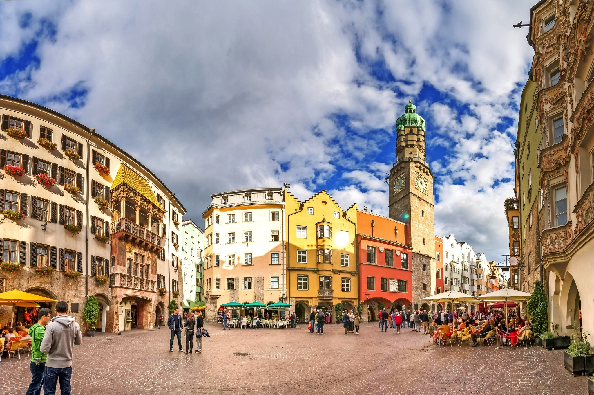 Historischer Platz mit bunten Gebäuden und einem Turm, Menschen spazieren.