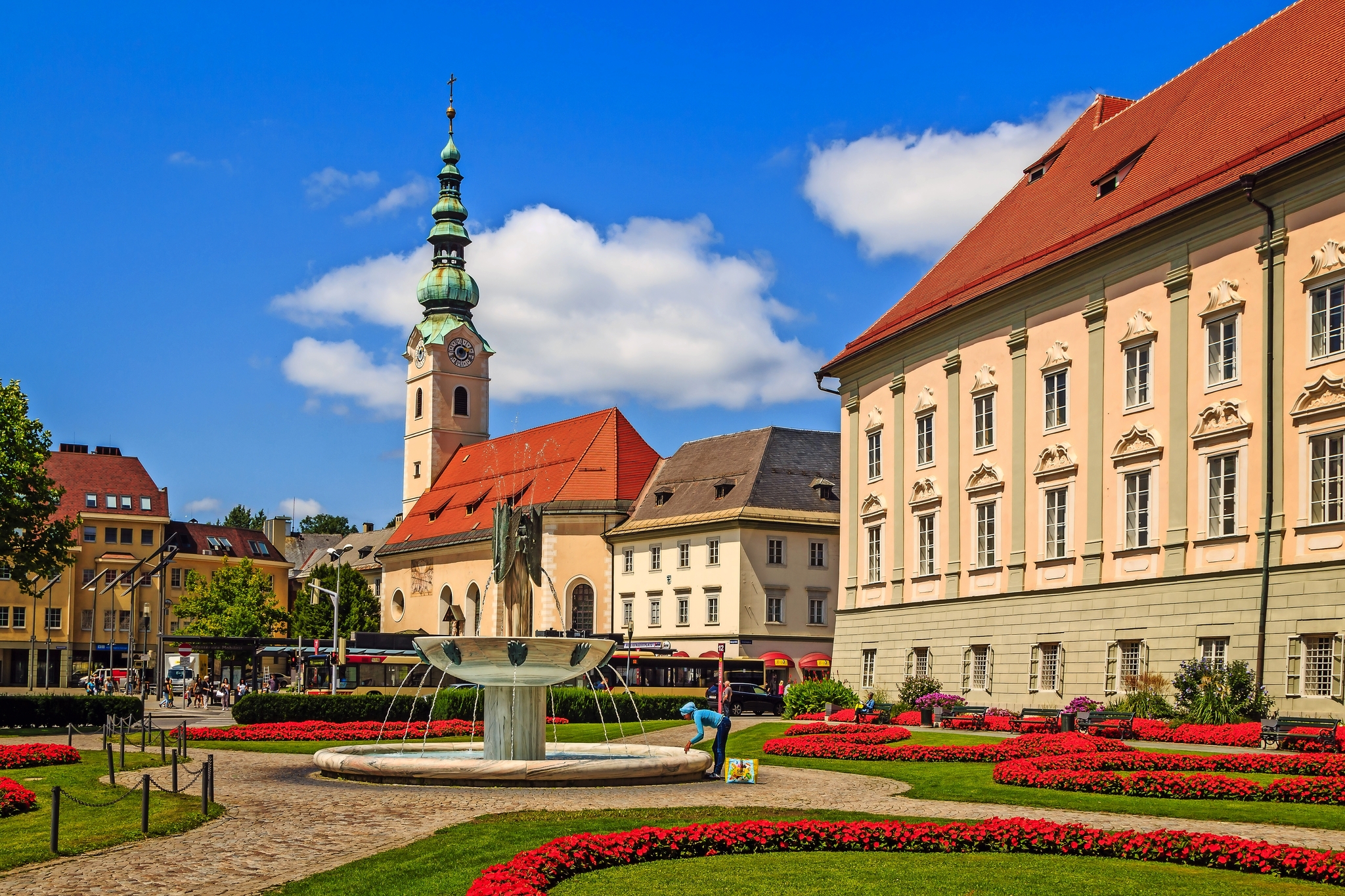 Stadtplatz mit Brunnen, Blumenbeeten und historischem Gebäude bei sonnigem Wetter
