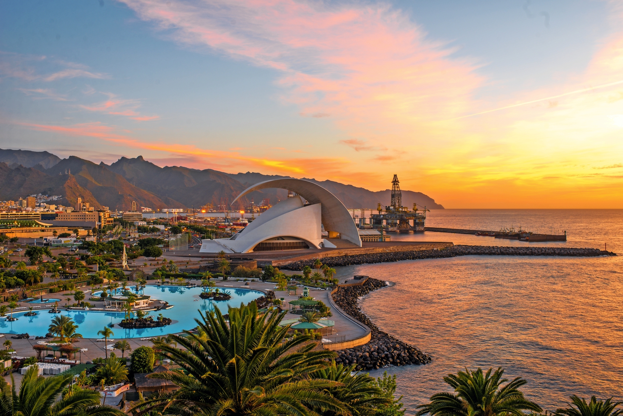 Küstenstadt bei Sonnenuntergang mit modernen Gebäuden und Palmen.