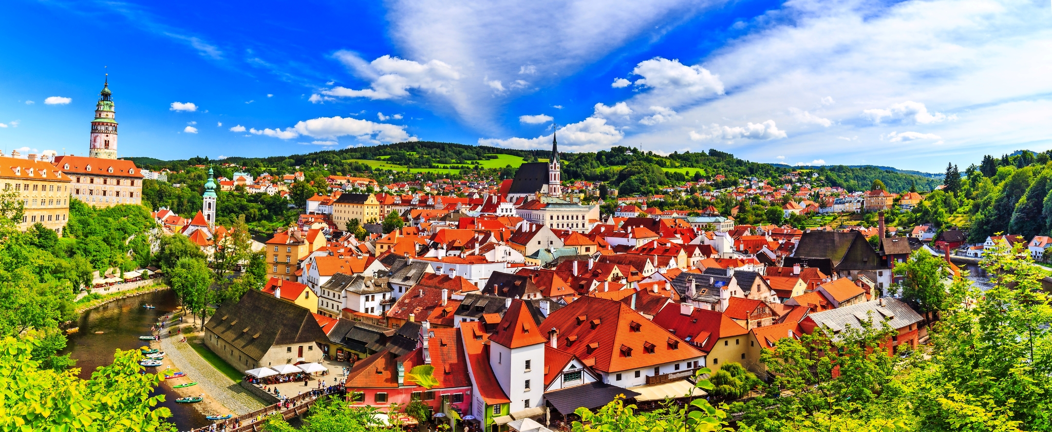 Panorama einer malerischen Stadt mit roten Dächern und Kirchturm im Grünen.