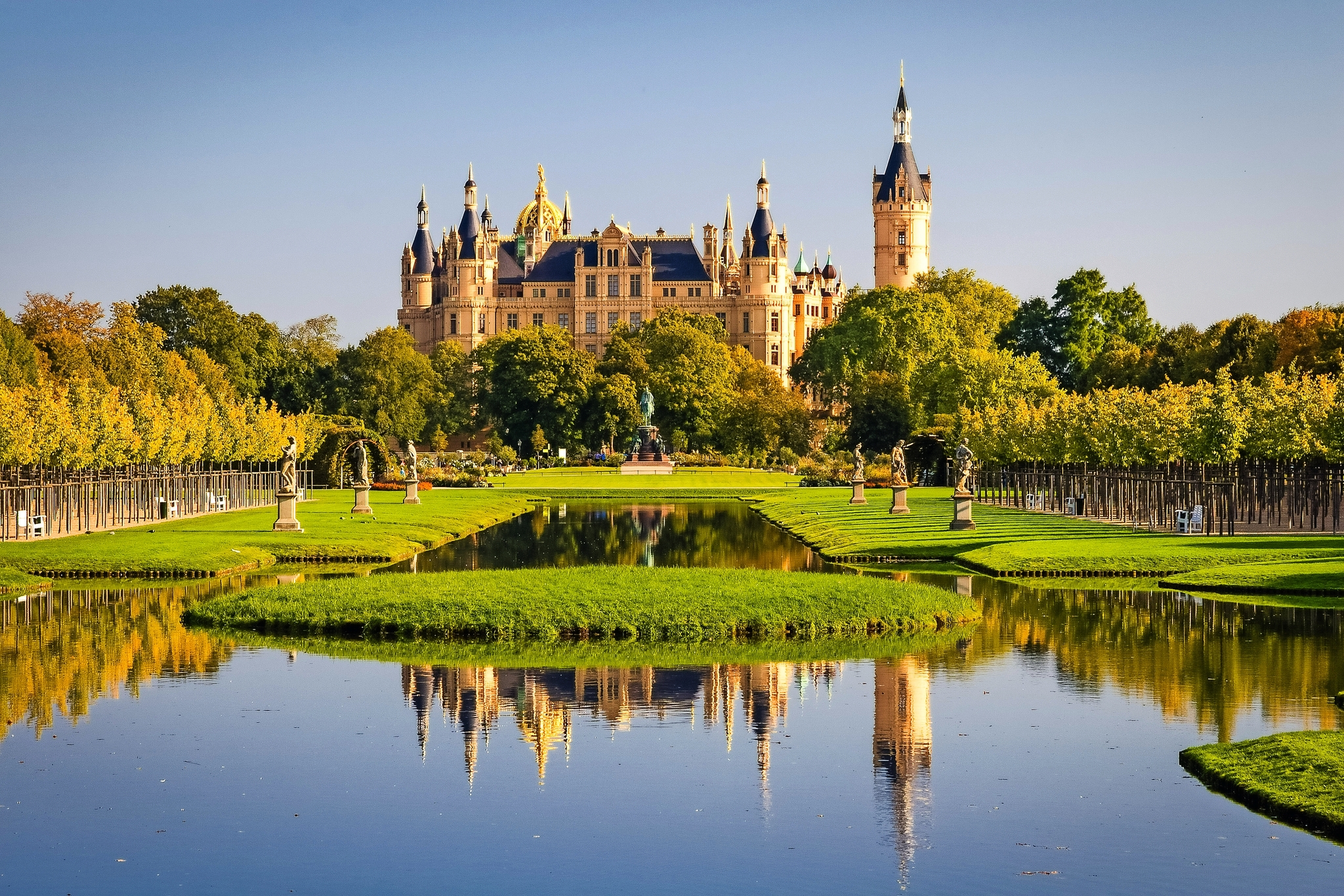 Schloss mit Garten und Teich im Vordergrund bei sonnigem Wetter