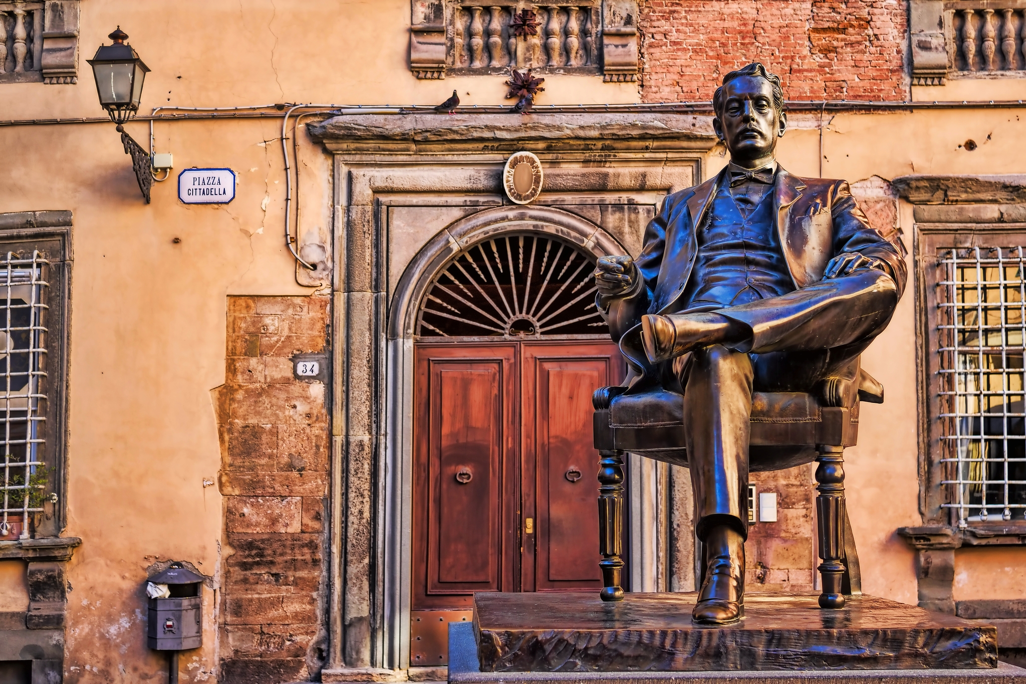 Villa Puccini Museum Bronzestatue eines sitzenden Mannes vor einem alten Gebäude mit Holztür.