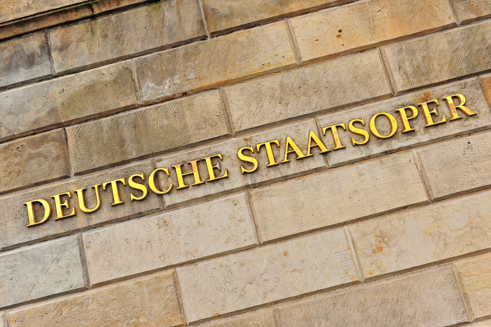 Deutsche Staatsoper in Berlin, Deutschland Deutsche Staatsoper in goldenen Buchstaben auf einer Steinmauer.