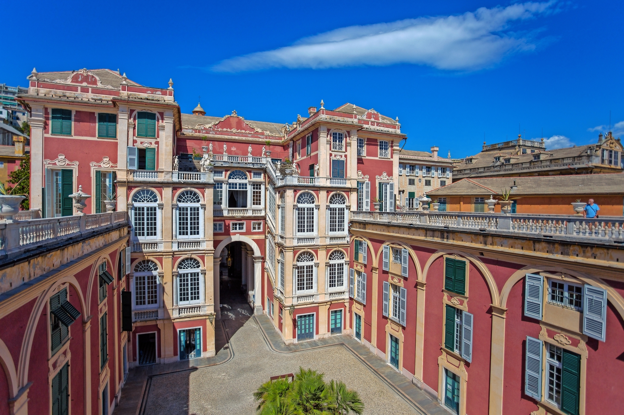Historisches Gebäude mit rosa Fassade und blauen Fensterläden unter blauem Himmel.