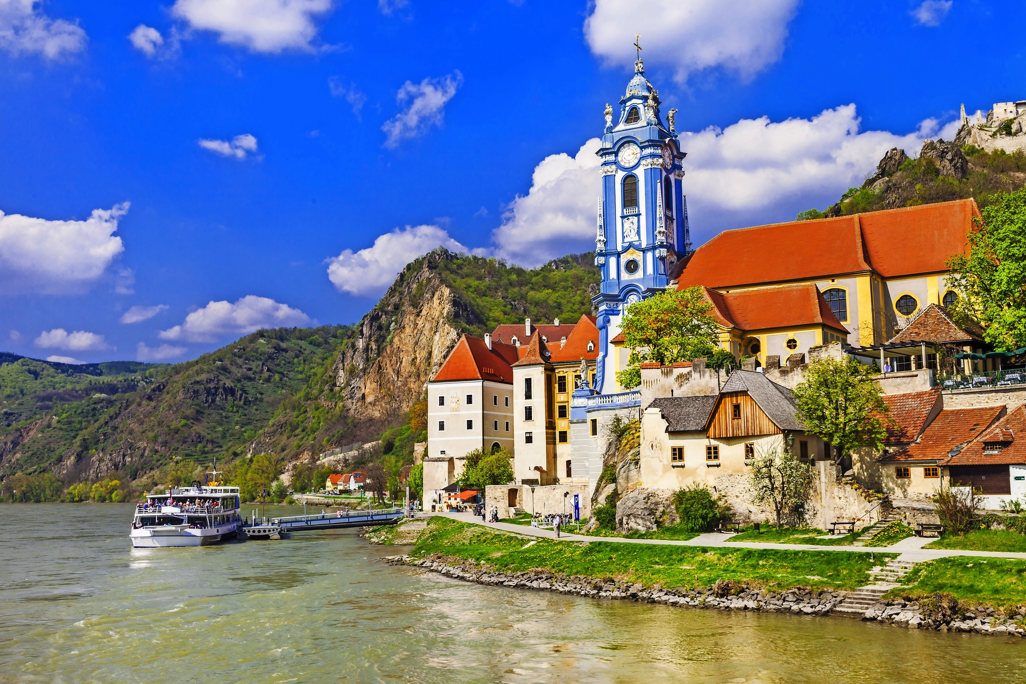 Blick auf die Stadt Dürnstein an der Donau mit einer Kirche und einem Ausflugsschiff.
