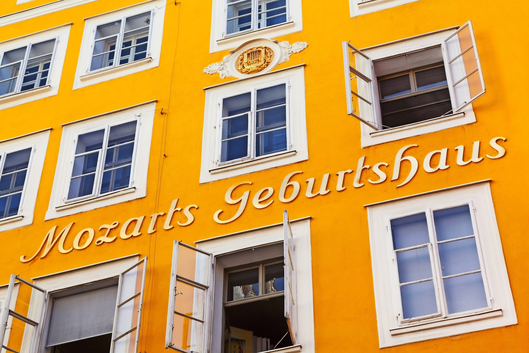 Gelbes Gebäude mit dem Schriftzug "Mozarts Geburtshaus" und mehreren geöffneten Fenstern.