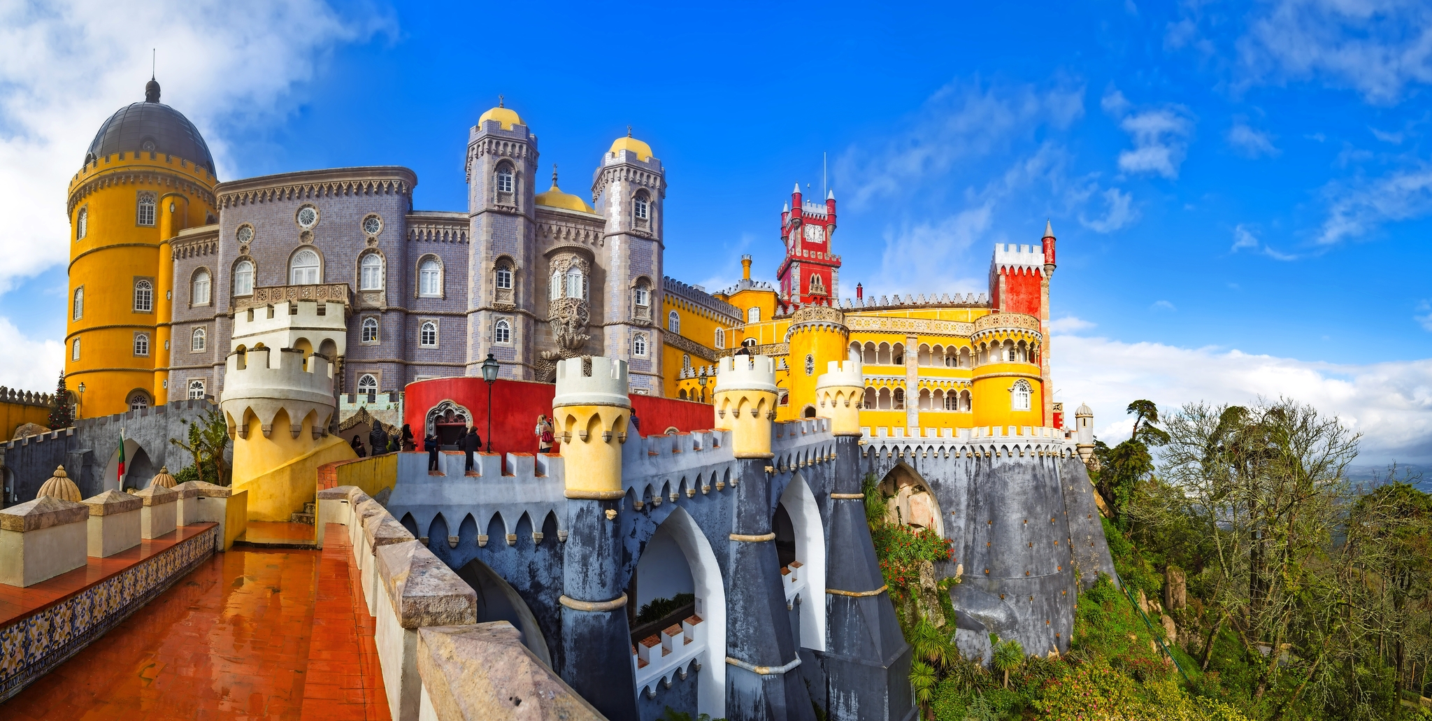 Buntes Schloss auf Hügel mit blauen Himmel und grüner Landschaft.