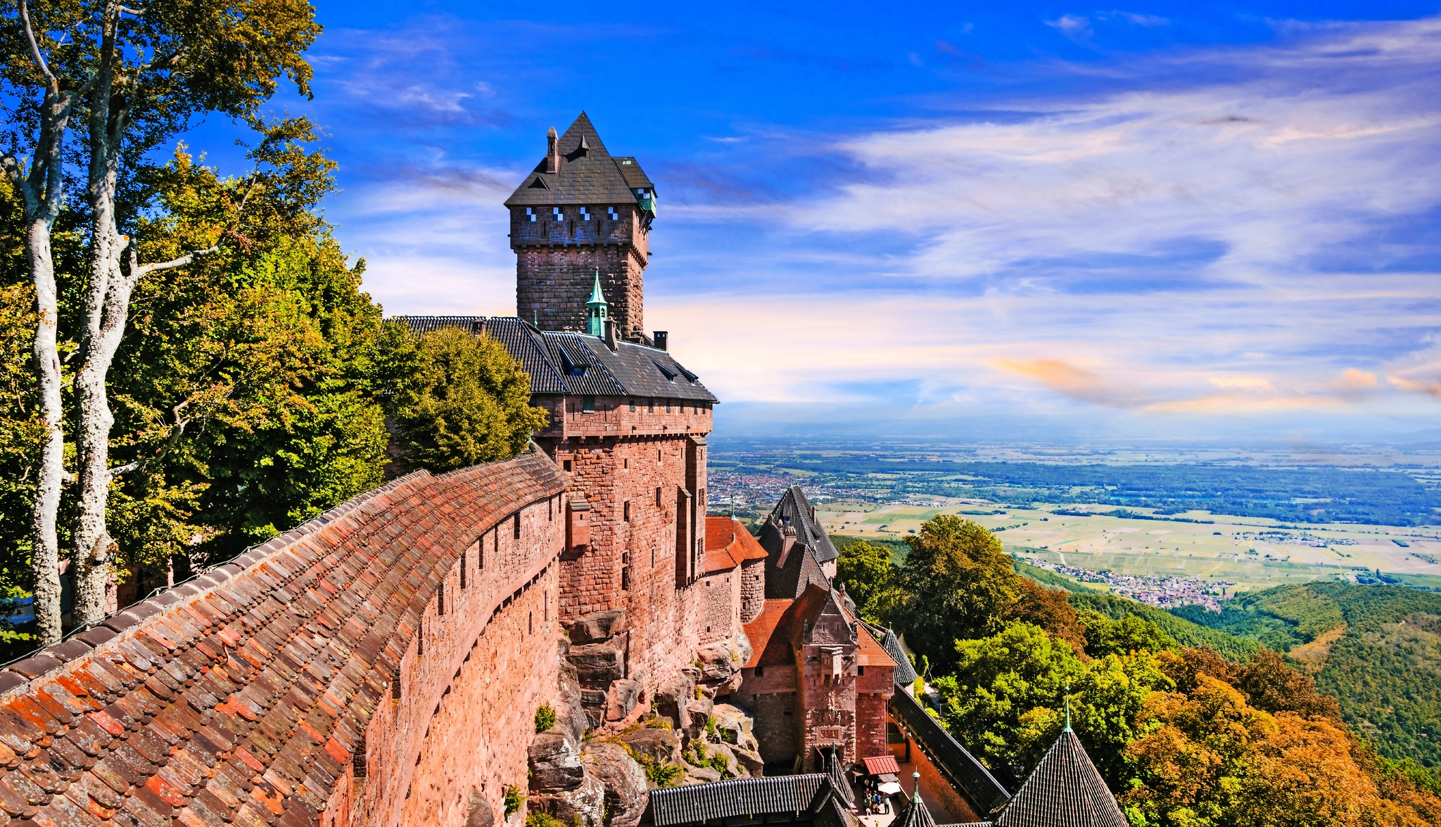 Mittelalterliche Burg umgeben von Bäumen und Landschaft im Hintergrund.