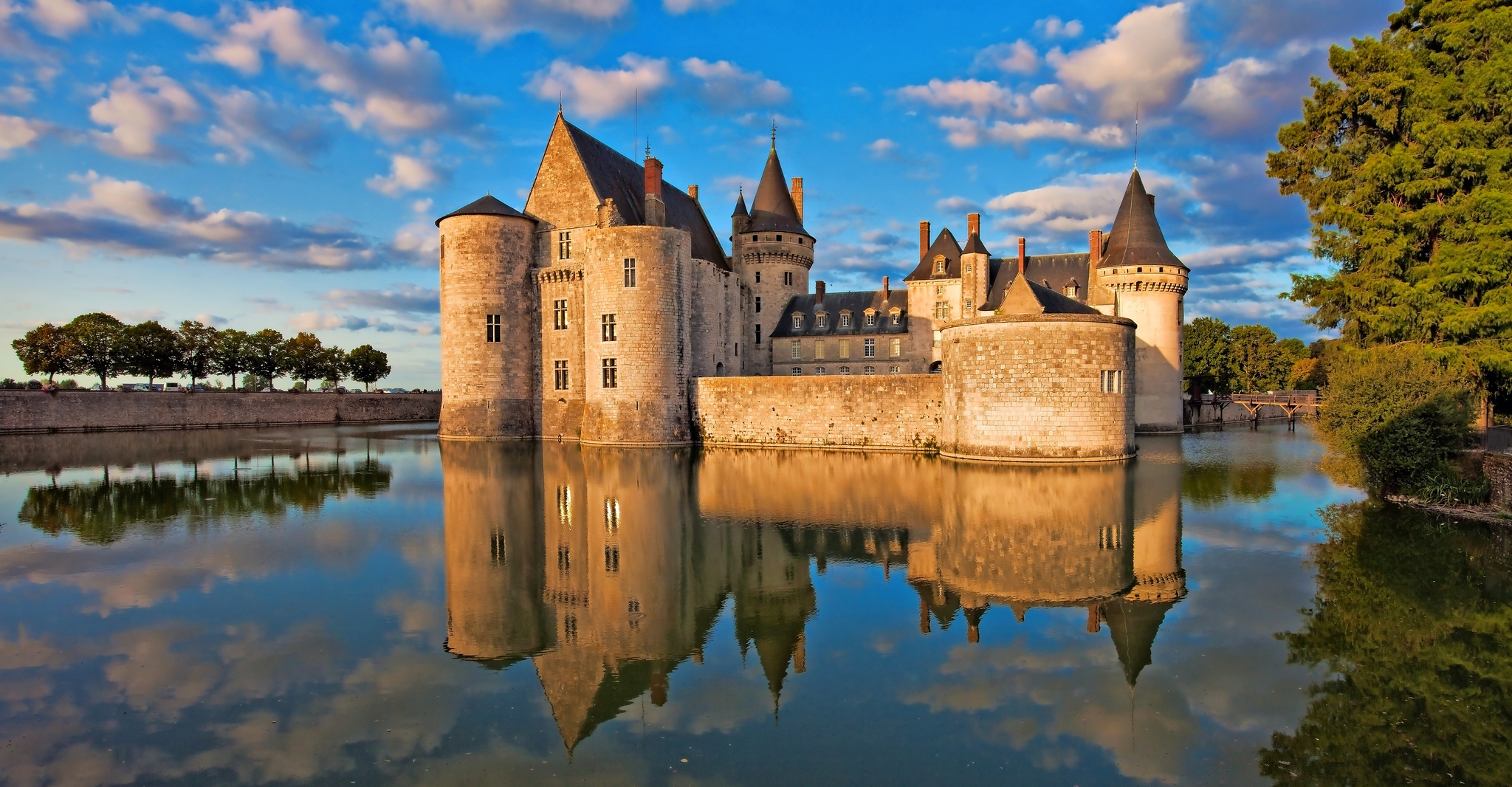 Mittelalterliche Burg reflektiert im Wasser, umgeben von Natur bei Sonnenuntergang.